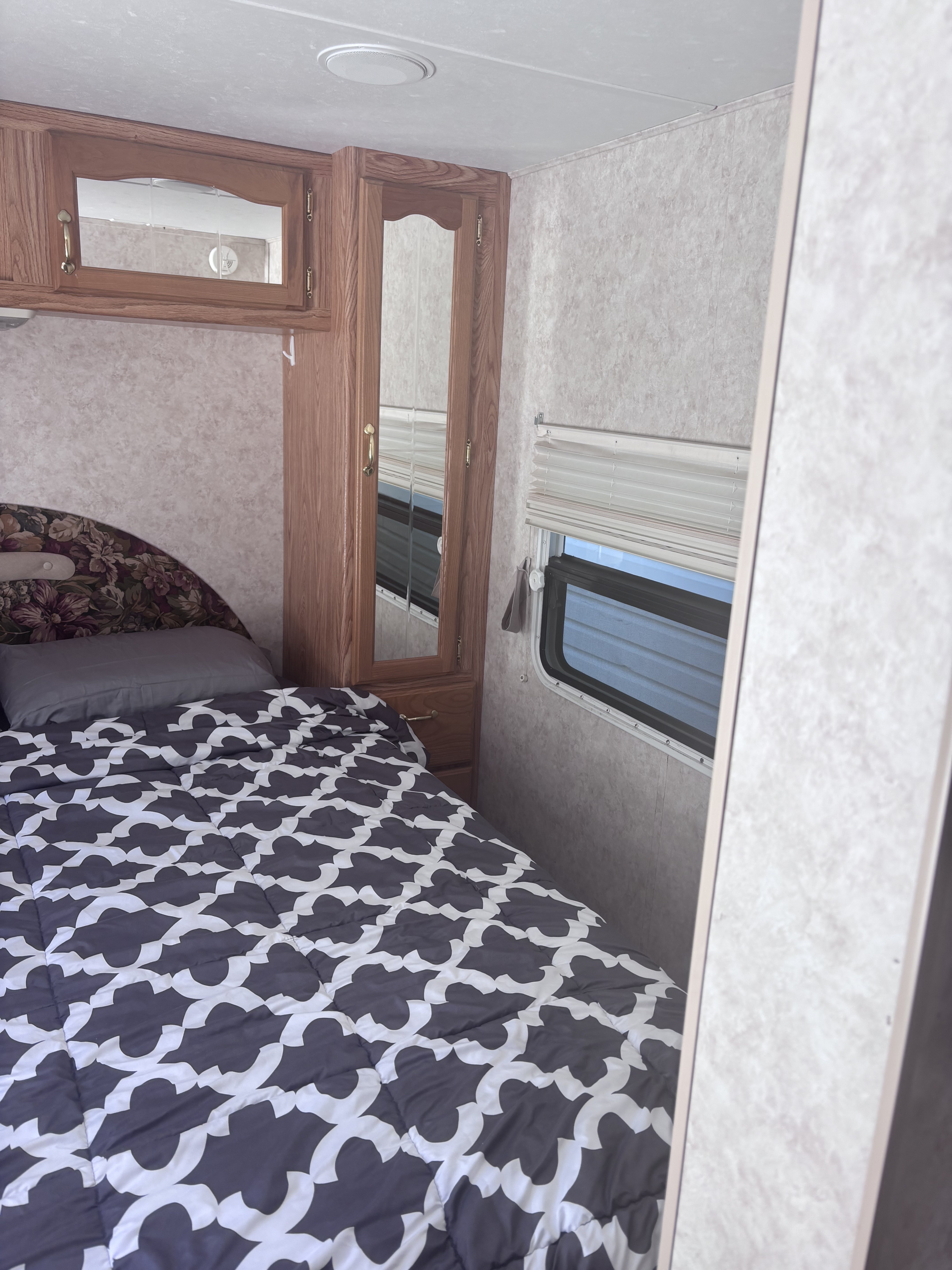 Cozy RV rental bedroom interior: floral headboard, patterned comforter, wood cabinetry, and window with blinds.. Cedar Creek Silverback 2004