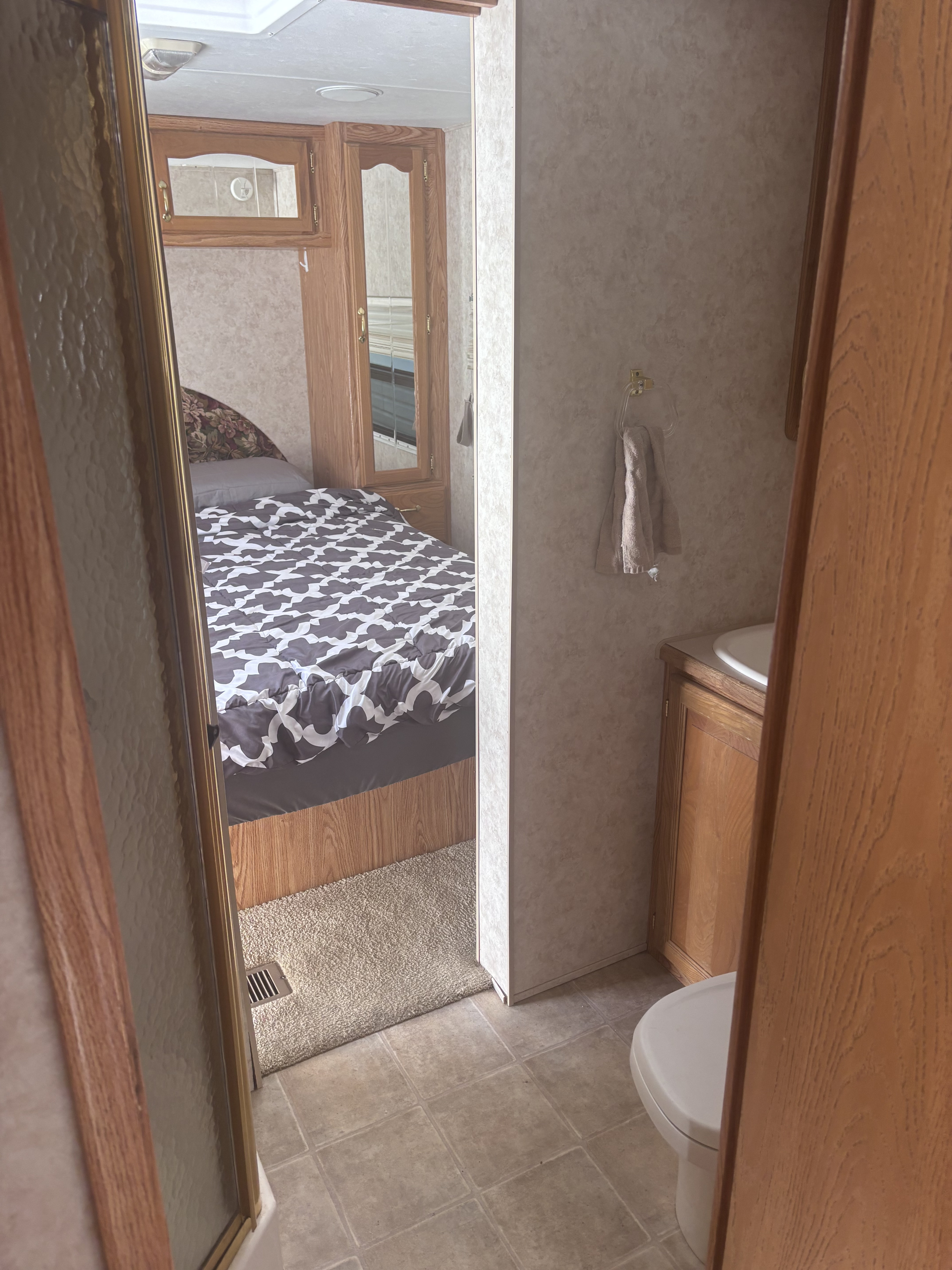 Inside this RV rental: a cozy bedroom with patterned bedding on the left, adjacent to a compact bathroom with toilet & sink.. Cedar Creek Silverback 2004