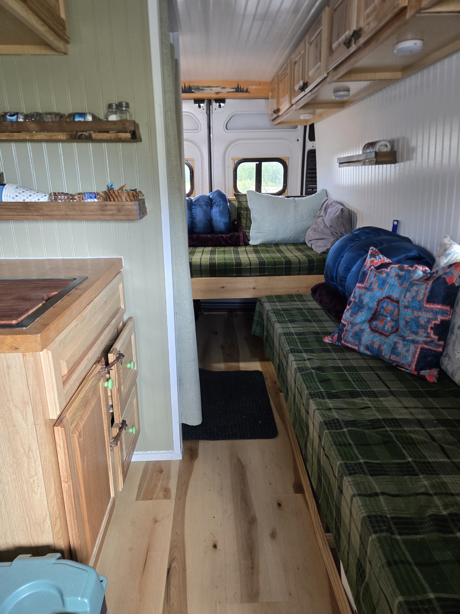 Cozy RV rental interior with custom wood kitchen, shelves, and comfortable green plaid sleeping areas.. Dodge Ram Pro Master 2500 2021