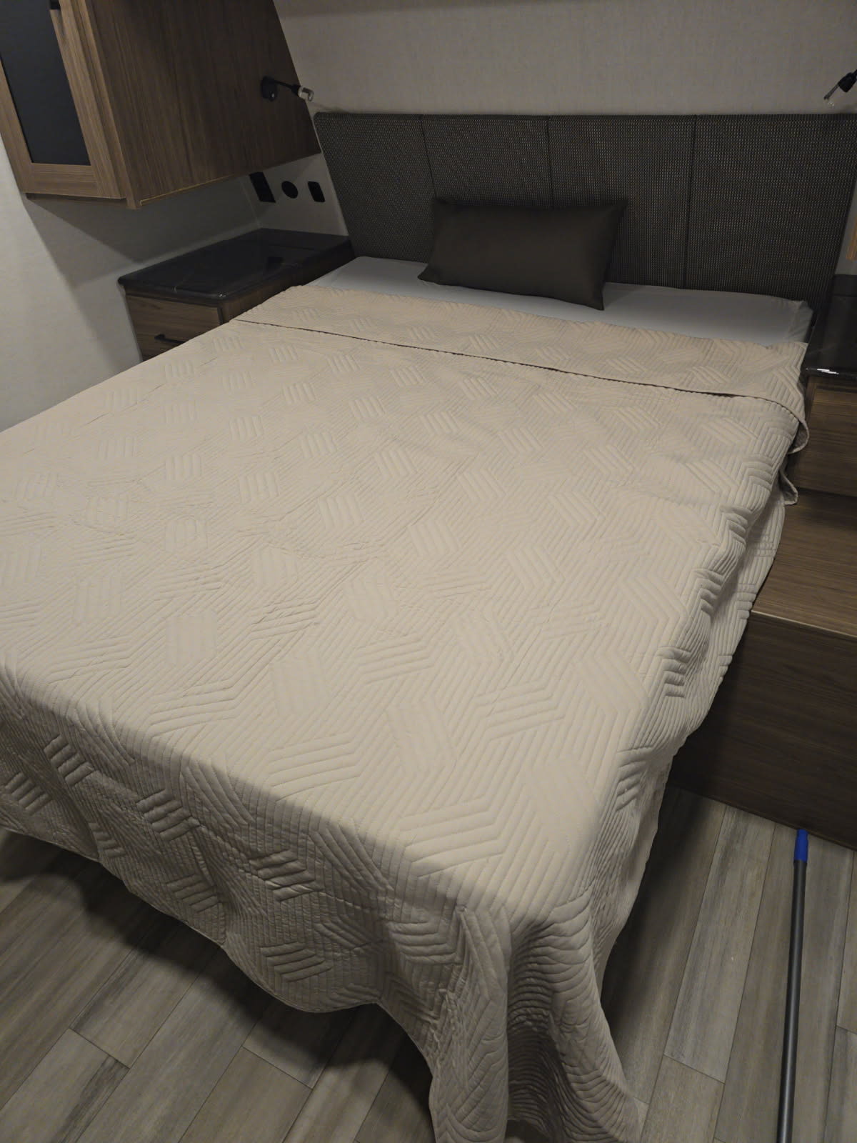 RV rental bedroom with a neatly made bed featuring a light, geometric quilted spread, dark headboard, and wood storage.. Alliance Delta 292RL 2025