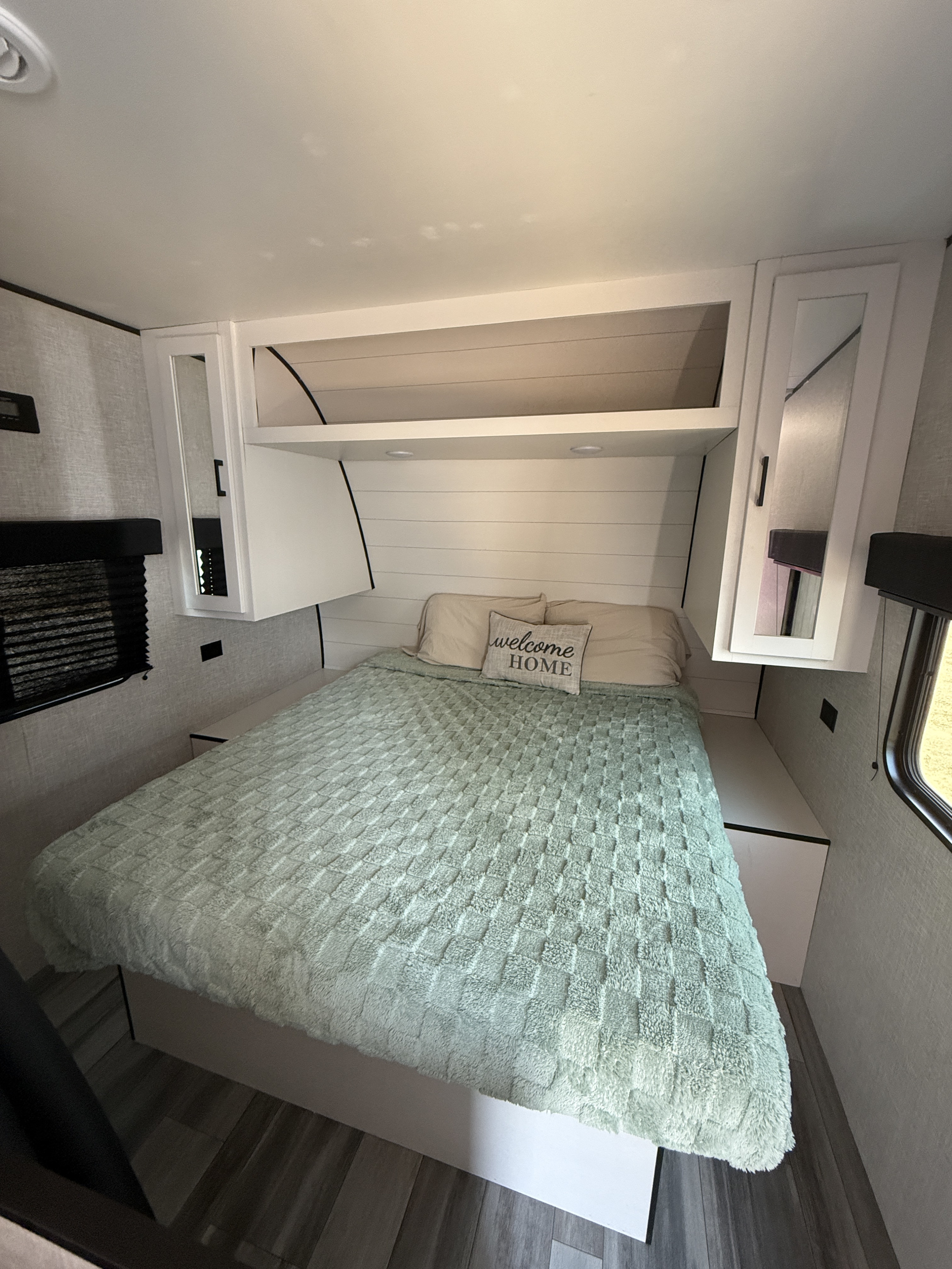 Cozy RV rental bedroom featuring a bed with a green blanket, pillows, and overhead storage.. Jayco Jay Flight SLX 2024