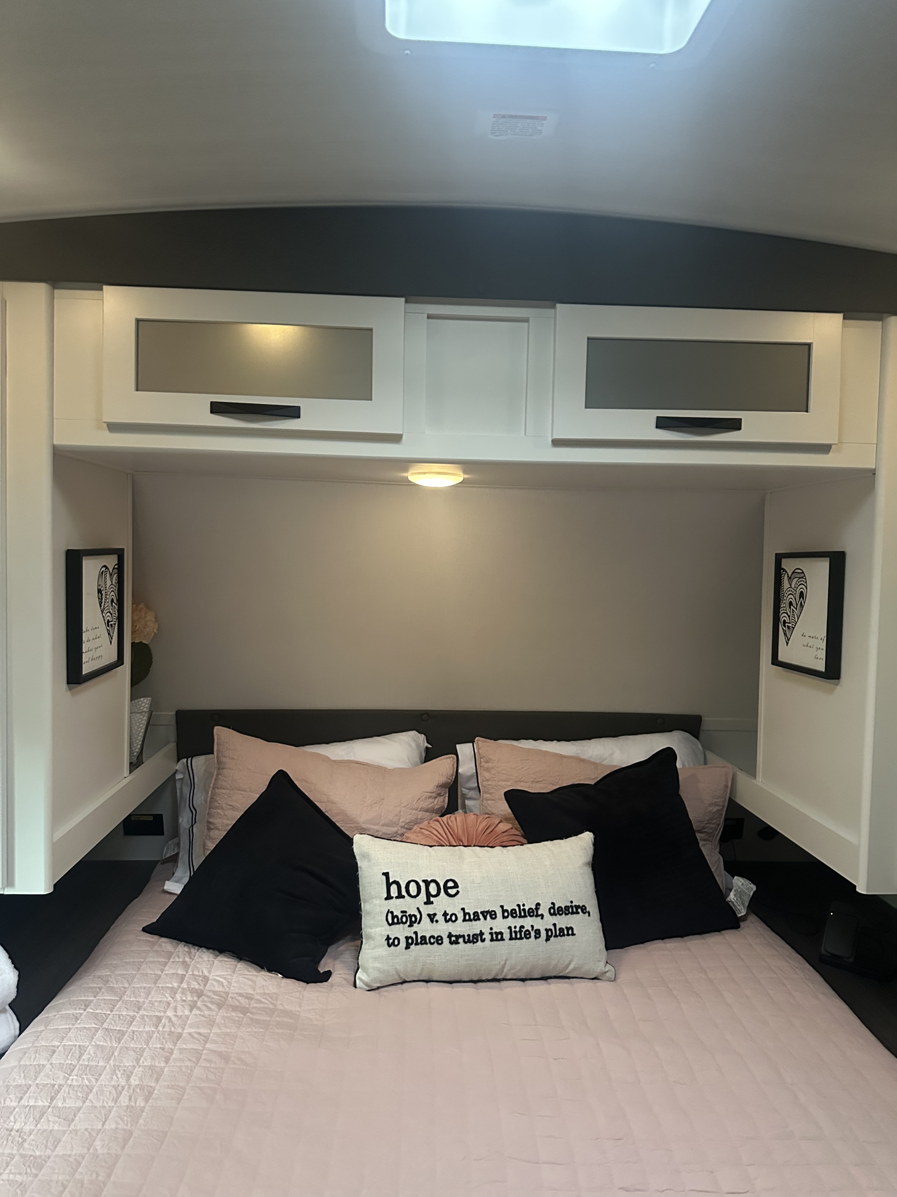 Cozy RV rental bedroom with coral blush quilt, "hope" pillow, and overhead cabinets for storage, offering a relaxing comfy space.. Keystone Passport 2025