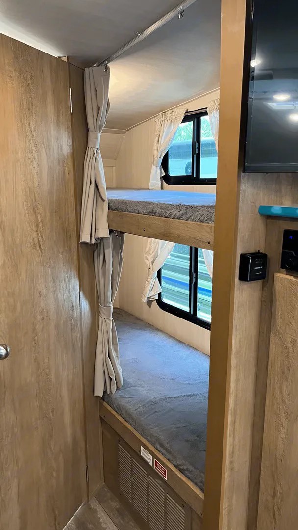An RV rental interior showing a dedicated sleeping area with two stacked bunk beds, each with privacy curtains and windows.. Gulf Stream Vintage Cruiser 2021