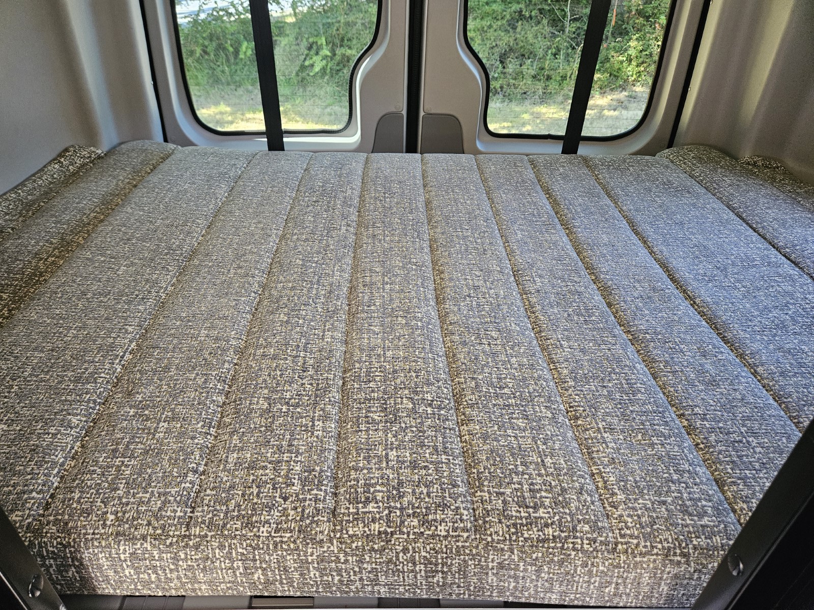 Cozy grey bed inside an RV rental camper van, ready for your next adventure.. Winnebago Revel 2018