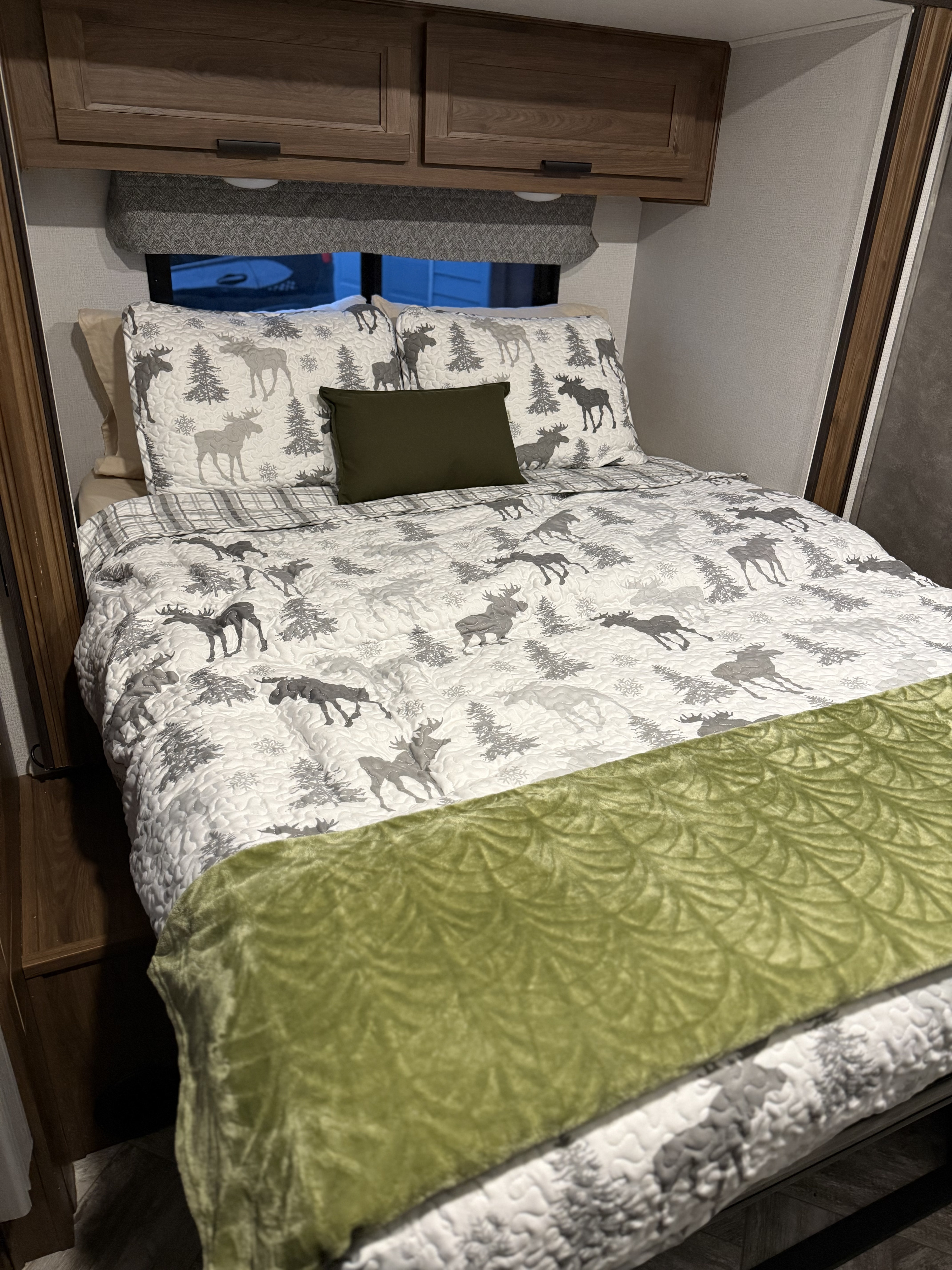 Relax in this RV rental's cozy bedroom featuring a moose-themed quilt, green throw, and wood-grain cabinets.. Forester LE 2022