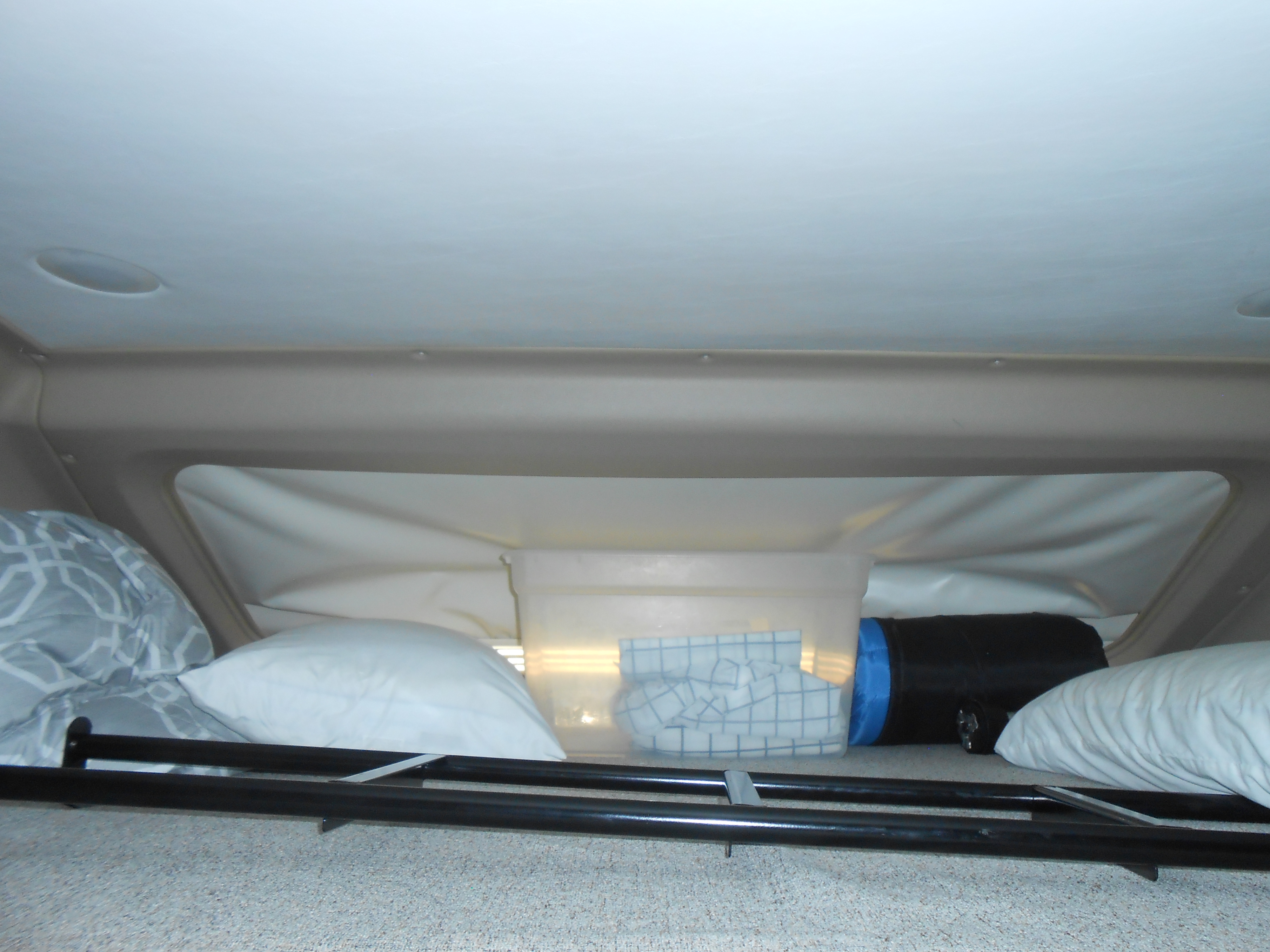 Inside an RV rental: a cozy cab-over bed area with pillows, a storage bin, and black safety rails.. Entegra Coach Qwest 2021