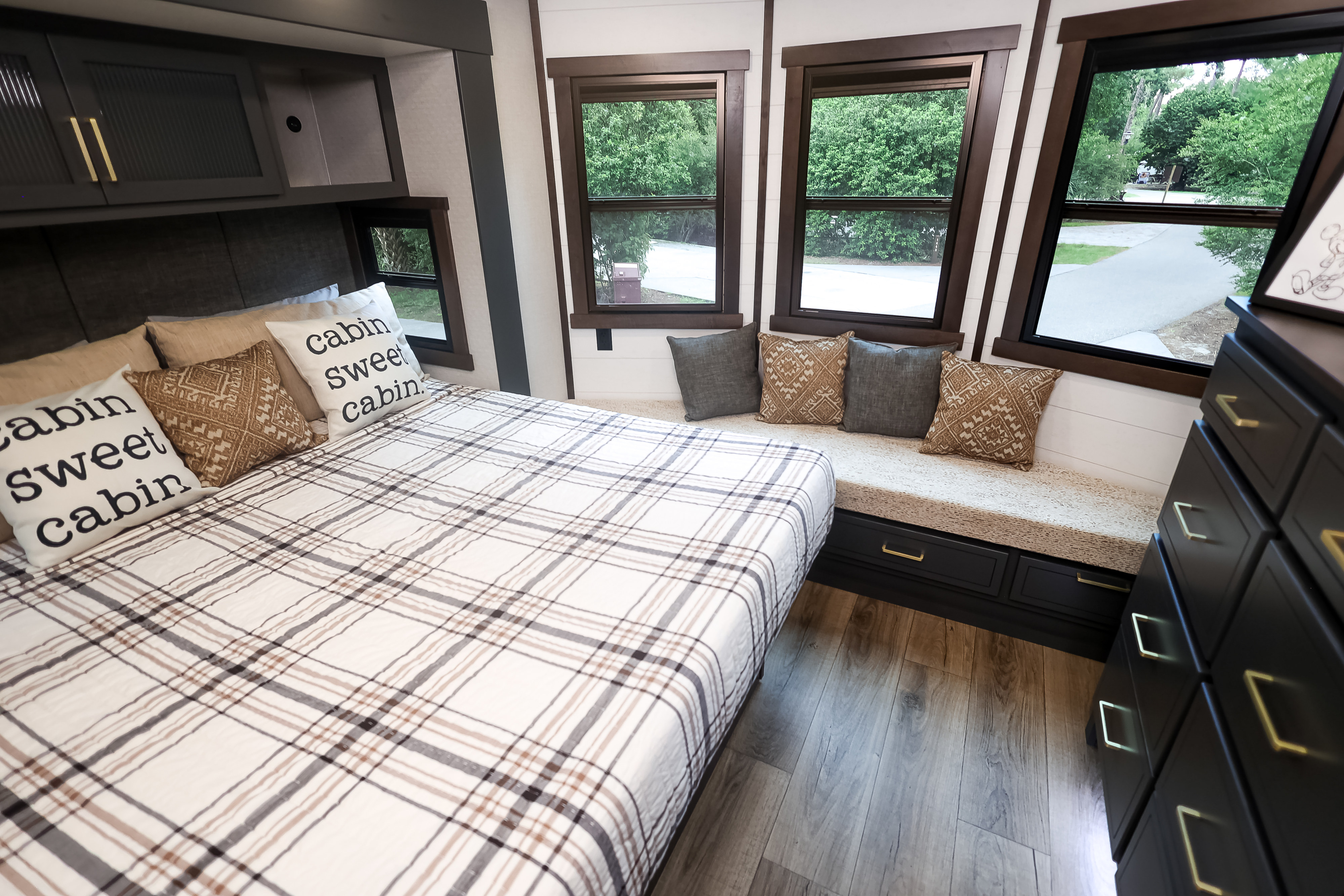 Spacious RV rental bedroom: comfy bed, 'cabin sweet cabin' pillows, built-in window seat, and smart storage.. Forest River Cedar Creek Cottage 2025