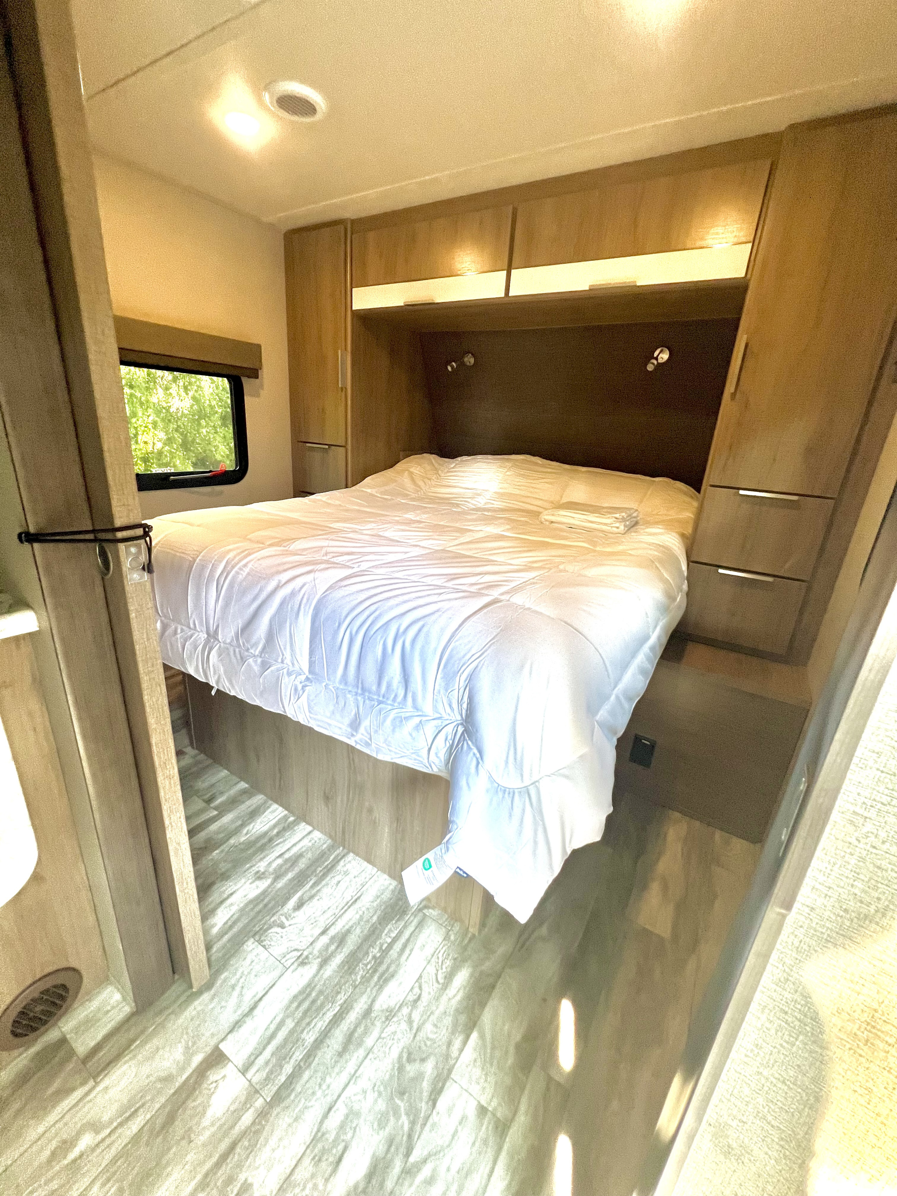 Spacious RV rental bedroom with modern wood interior, comfy bed, and natural light.. Grand Design Imagine XLS 2021