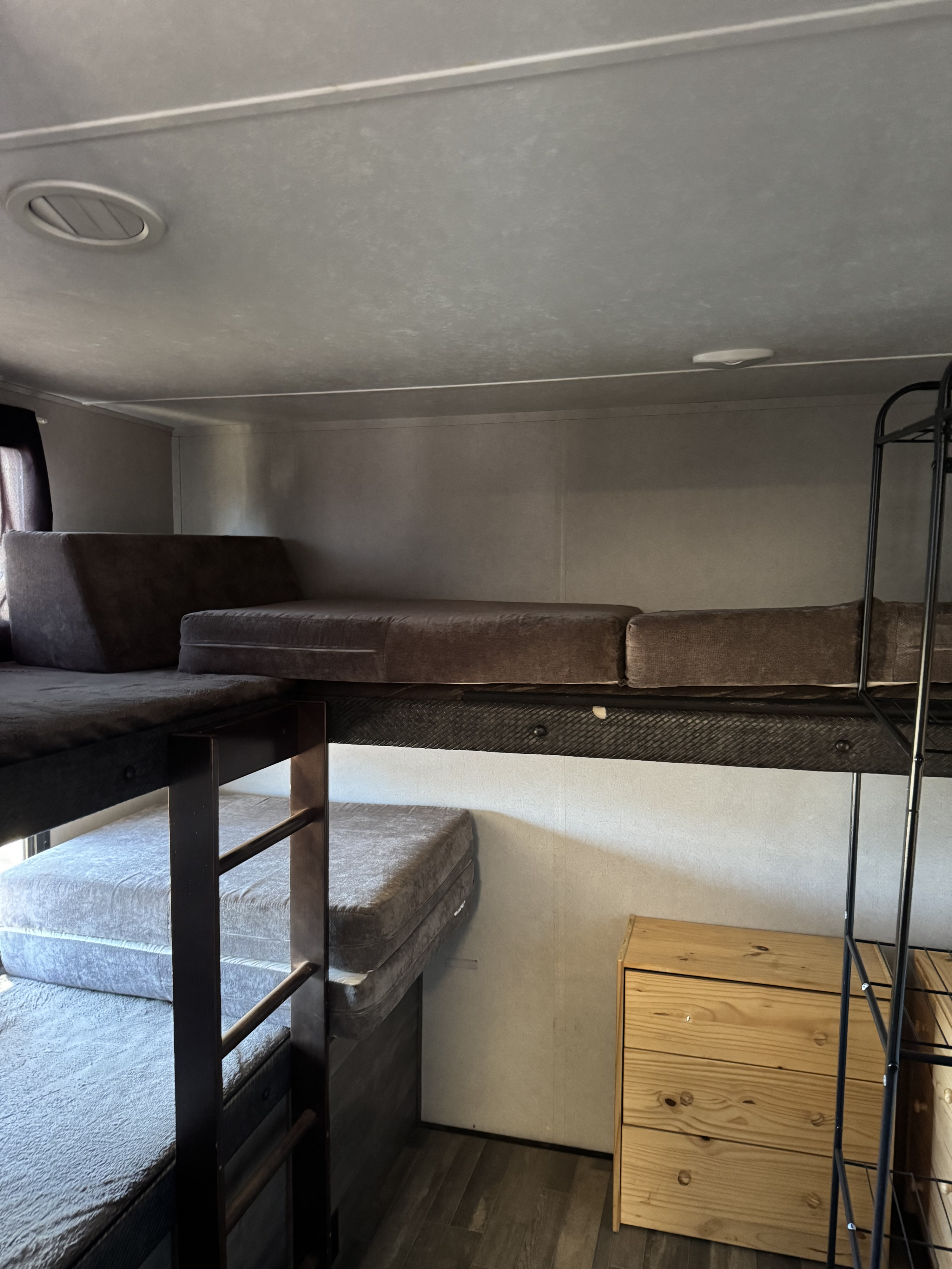 An RV rental interior featuring stacked bunk beds with cushions, a wood dresser, and metal shelving.. Forest River vibe 2020