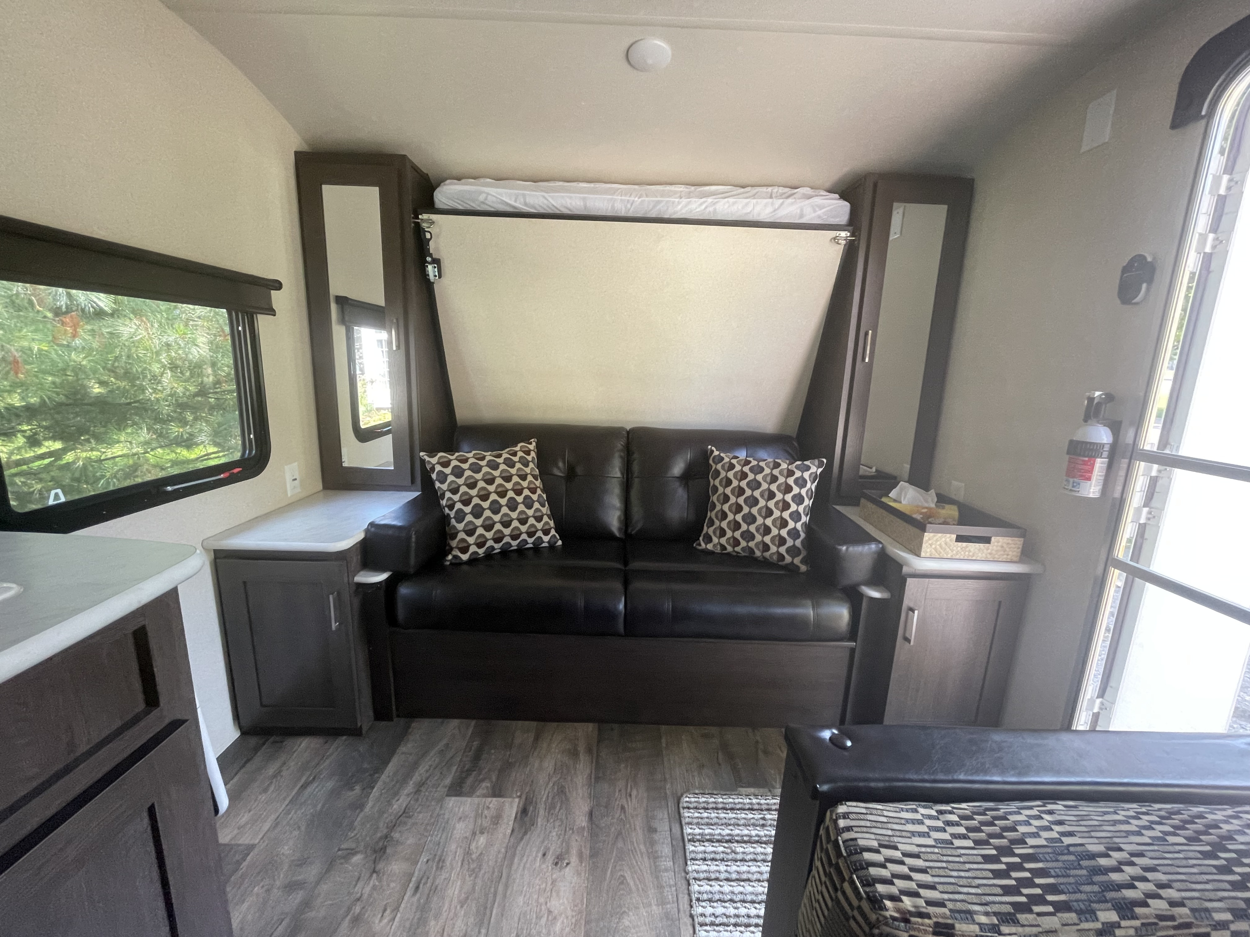 RV rental interior: compact living space with a black sofa, wall-mounted murphy bed (up), and storage cabinets.. Forest River Wildwood X-Lite 2018