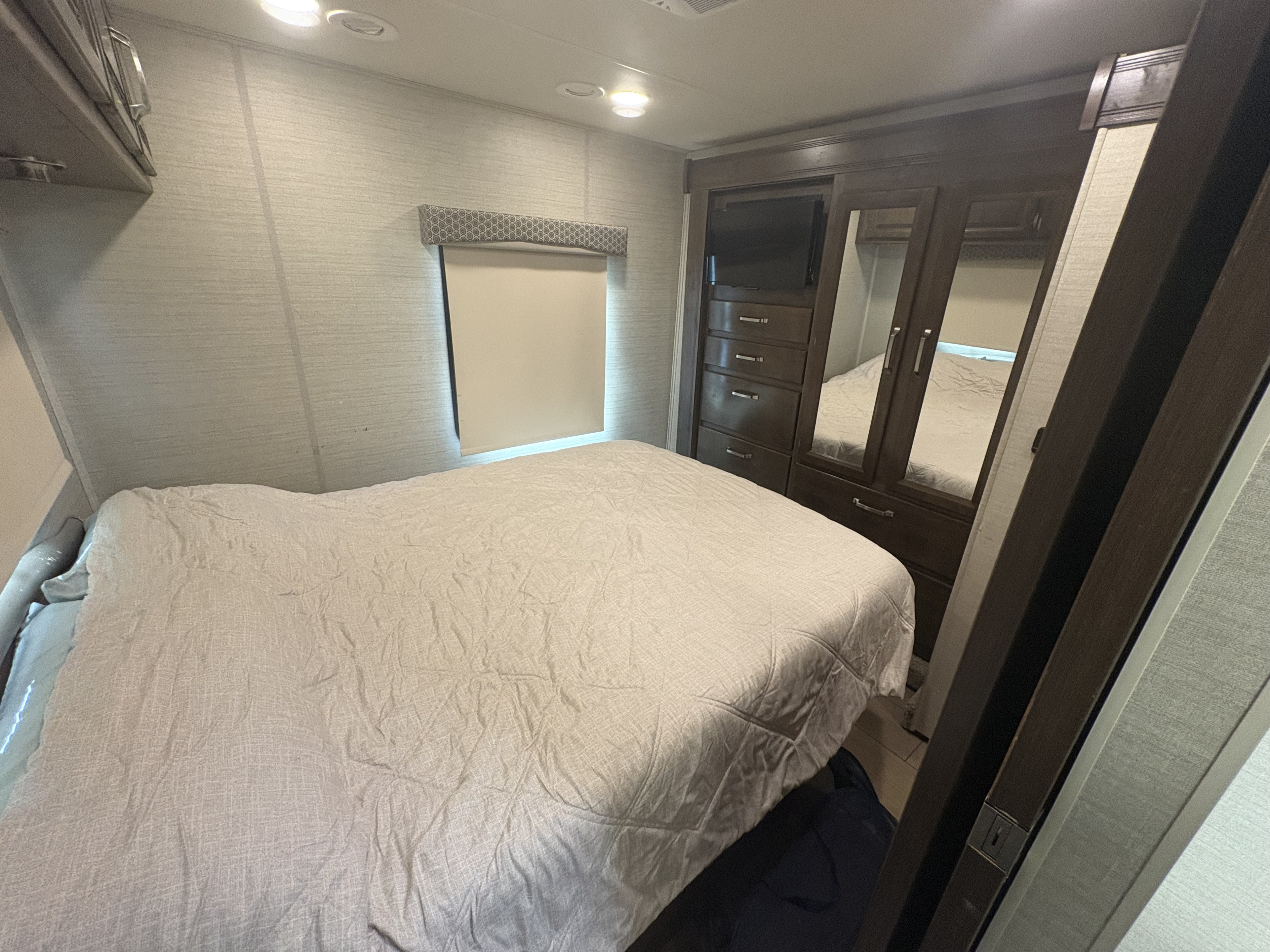 Experience comfort in this RV rental's spacious bedroom, featuring a large bed, TV, and mirrored wardrobe for your travels.. Jayco Greyhawk 2019