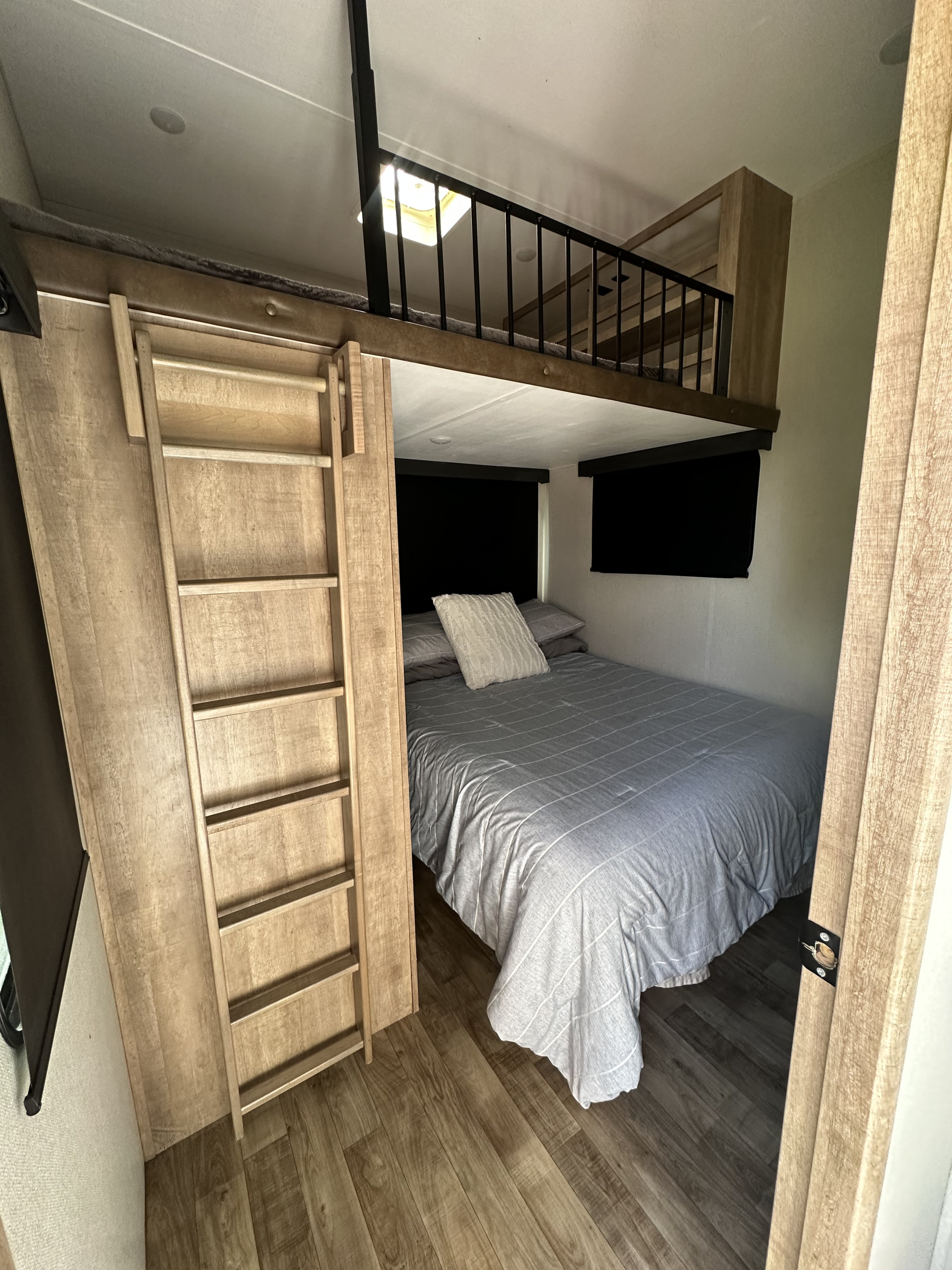 Bright RV rental interior showing a bedroom with a striped bed, black-railed loft, and wooden ladder for access.. Keystone RV Arcadia 3/4 Ton 2023