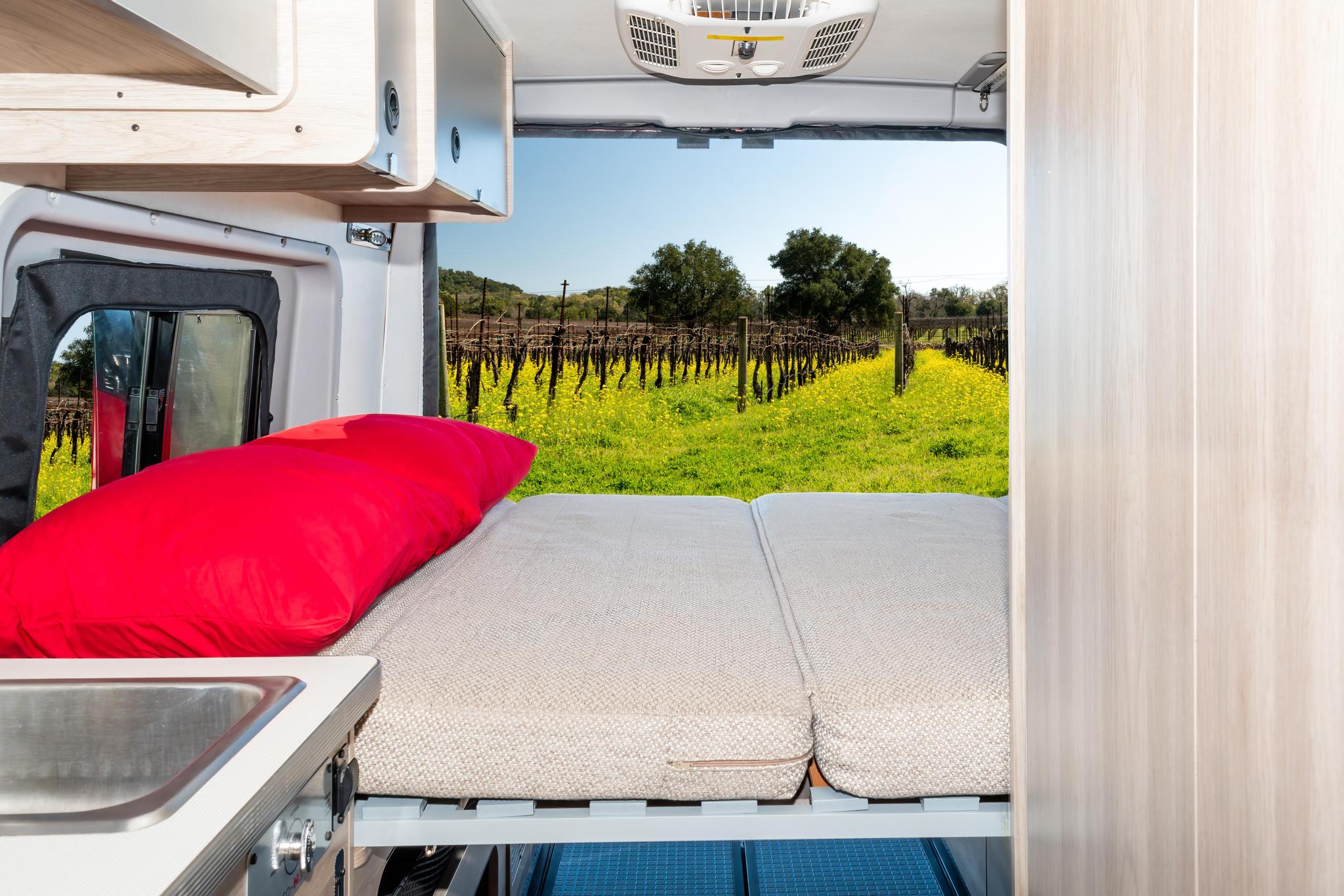 Cozy RV rental interior: bed, sink, and stunning vineyard view from the open back doors.. Winnebago Solis 2023