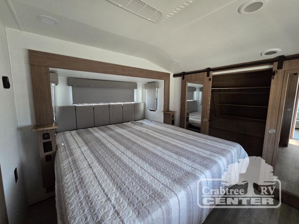 RV rental interior: A bright bedroom with a large bed, padded headboard, wood accents, and mirrored closet doors.. Alliance Avenue 32RLS 2024