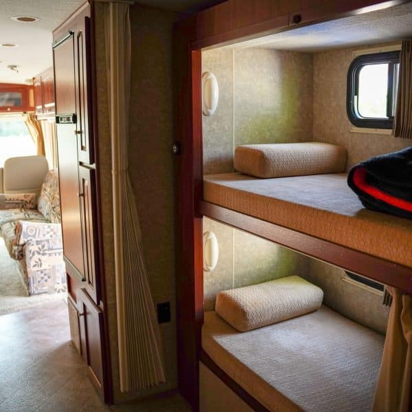 RV rental interior: A hallway leads to patterned seating, while bunk beds with pillows and a window offer compact comfort.. Winnebago Vista 2009