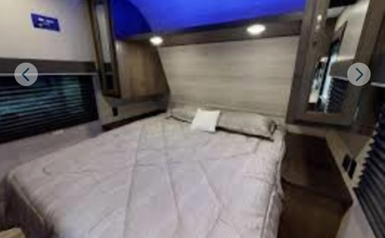 Cozy RV rental bedroom with a comfy bed, ambient blue lighting, window with blinds, and bedside mirror.. Jayco Jay Flight 2021