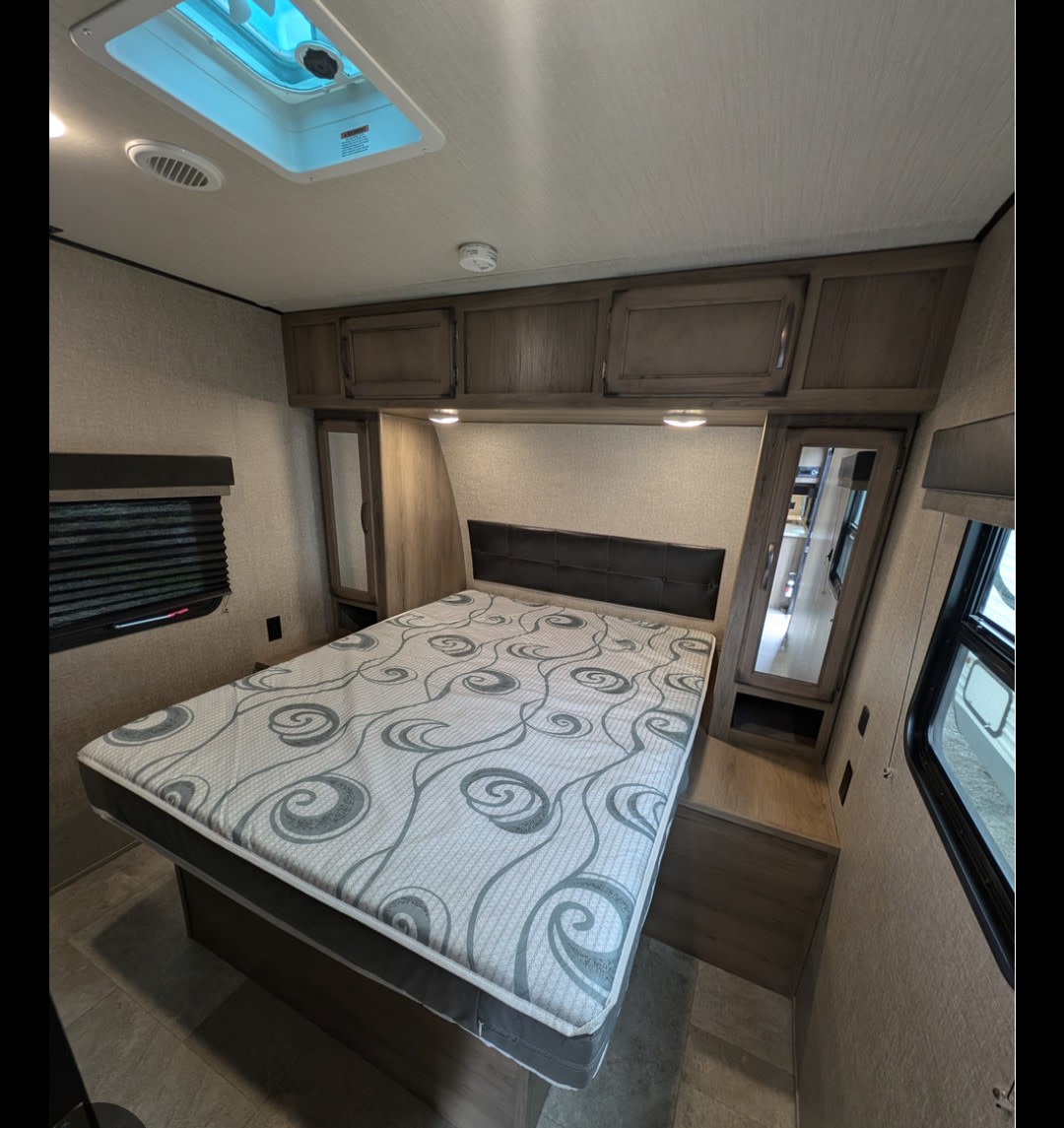 Cozy RV rental bedroom featuring a comfortable bed with patterned mattress, overhead storage, and a skylight.. Design Recreation Travel By Desgin 2020