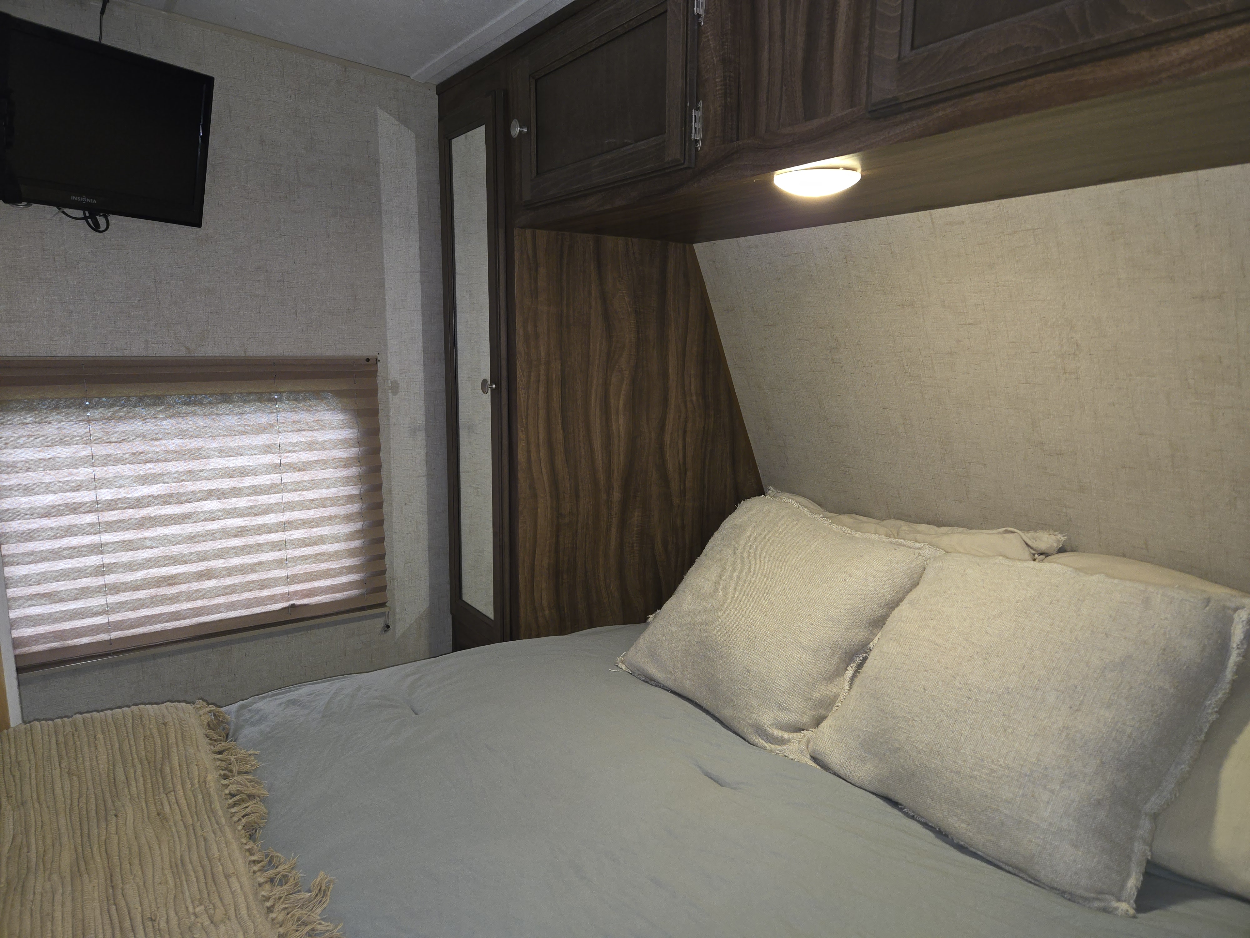 Cozy RV rental bedroom with a made bed, overhead storage, wall-mounted TV, and window blinds.. KZ Sportmen Sportster Toyhauler 2015