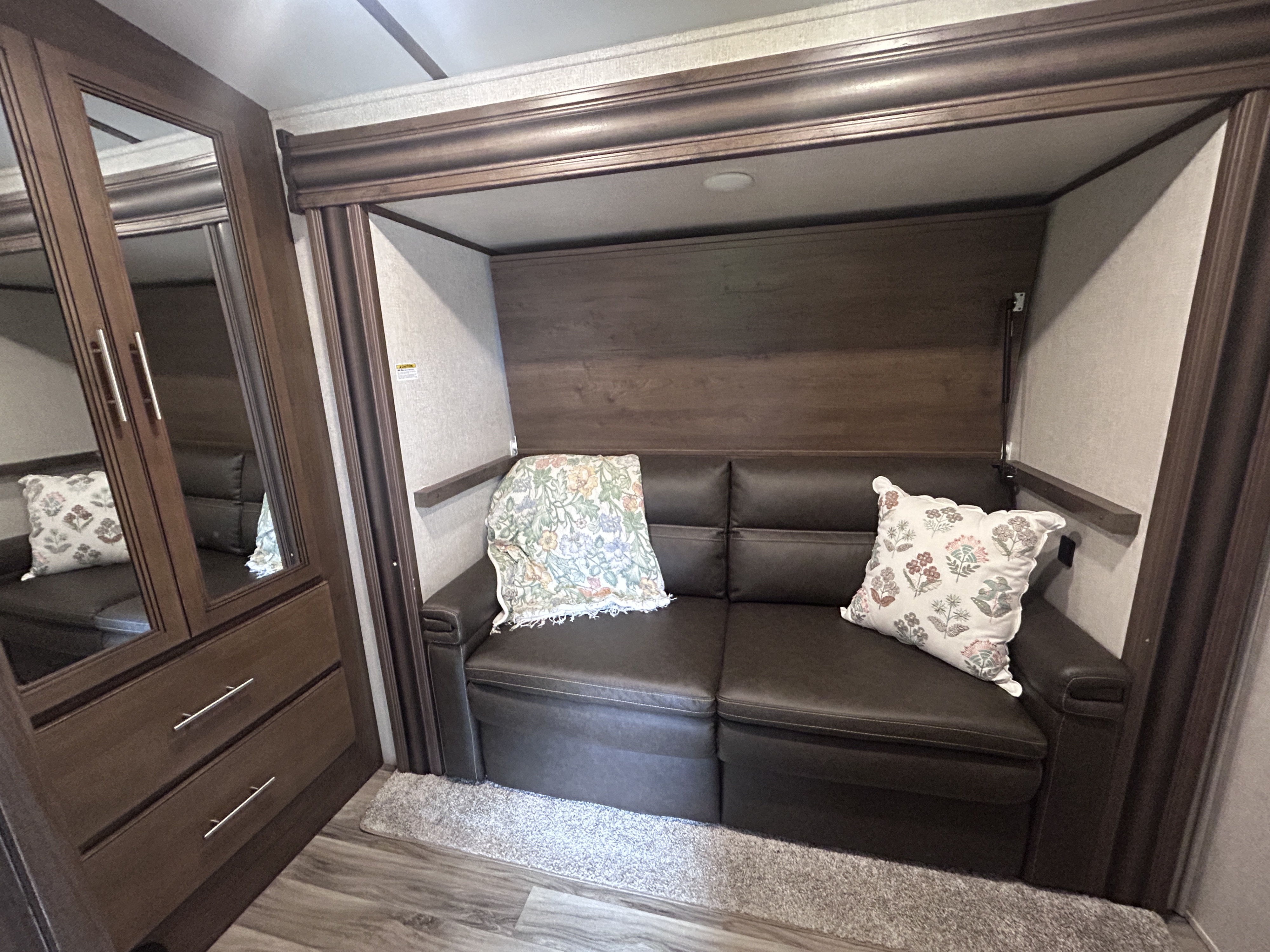 Experience an RV rental: a compact interior with a dark sofa, patterned pillows, and mirrored cabinets for comfortable travel.. Keystone RV Cougar 2021