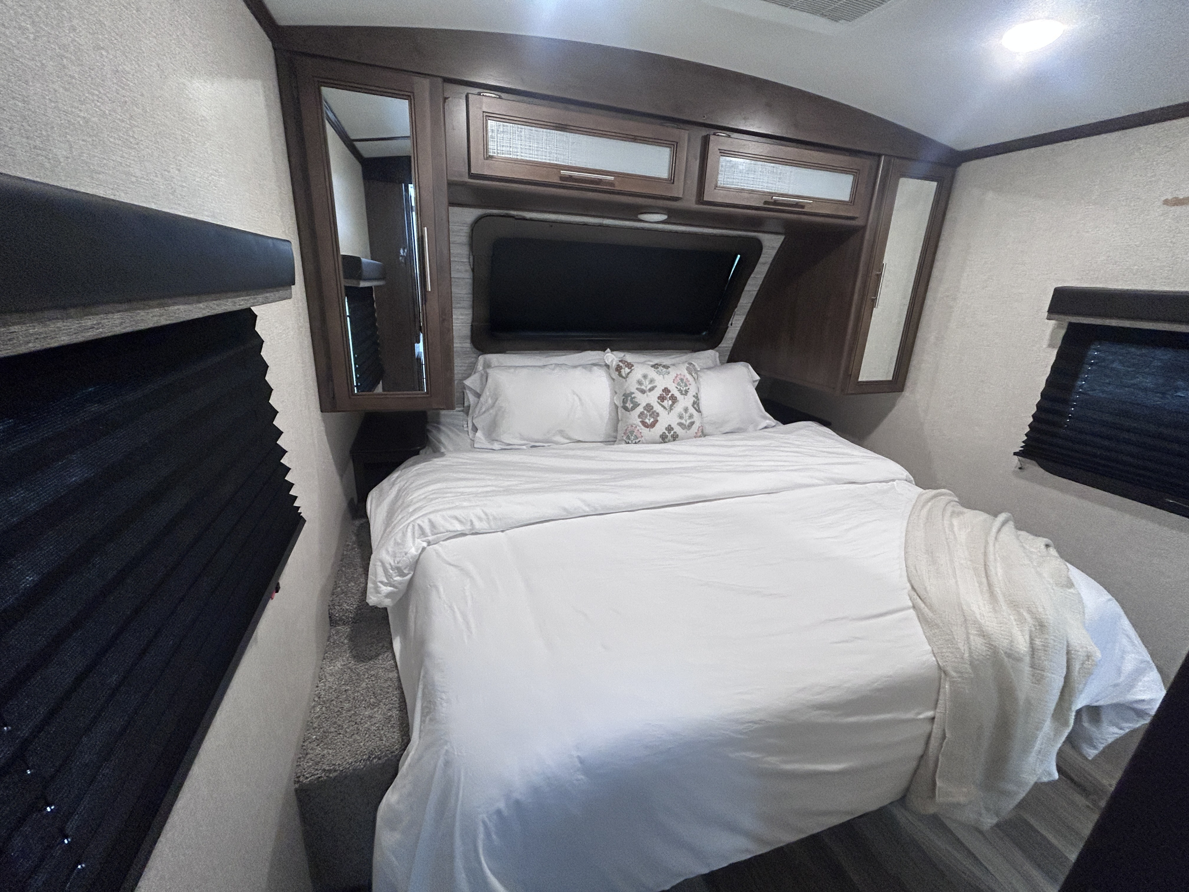 Experience comfort in this cozy RV rental bedroom featuring a queen bed with white linens, overhead storage, and privacy blinds.. Keystone RV Cougar 2021