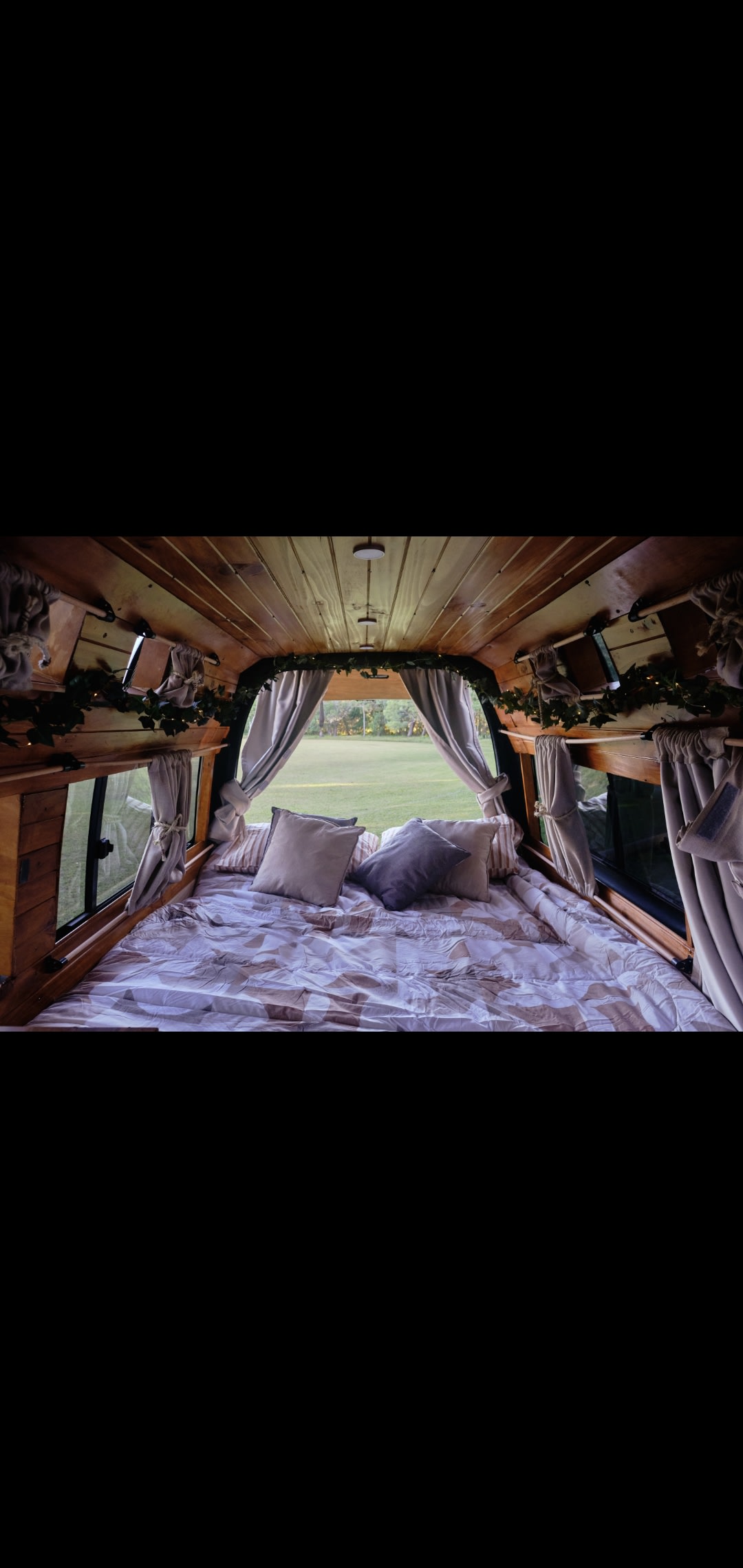 Cozy RV rental: A bed in a wood-paneled camper with curtains open to a serene green field view.. Toyota HIACE 2007
