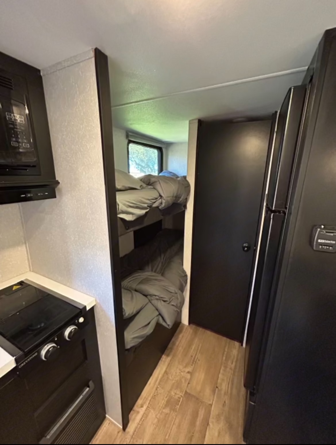 An RV rental interior showing bunk beds, a compact kitchen with stovetop & microwave, and a fridge.. Forest River Cherokee Wolf Pup Black Label 2021