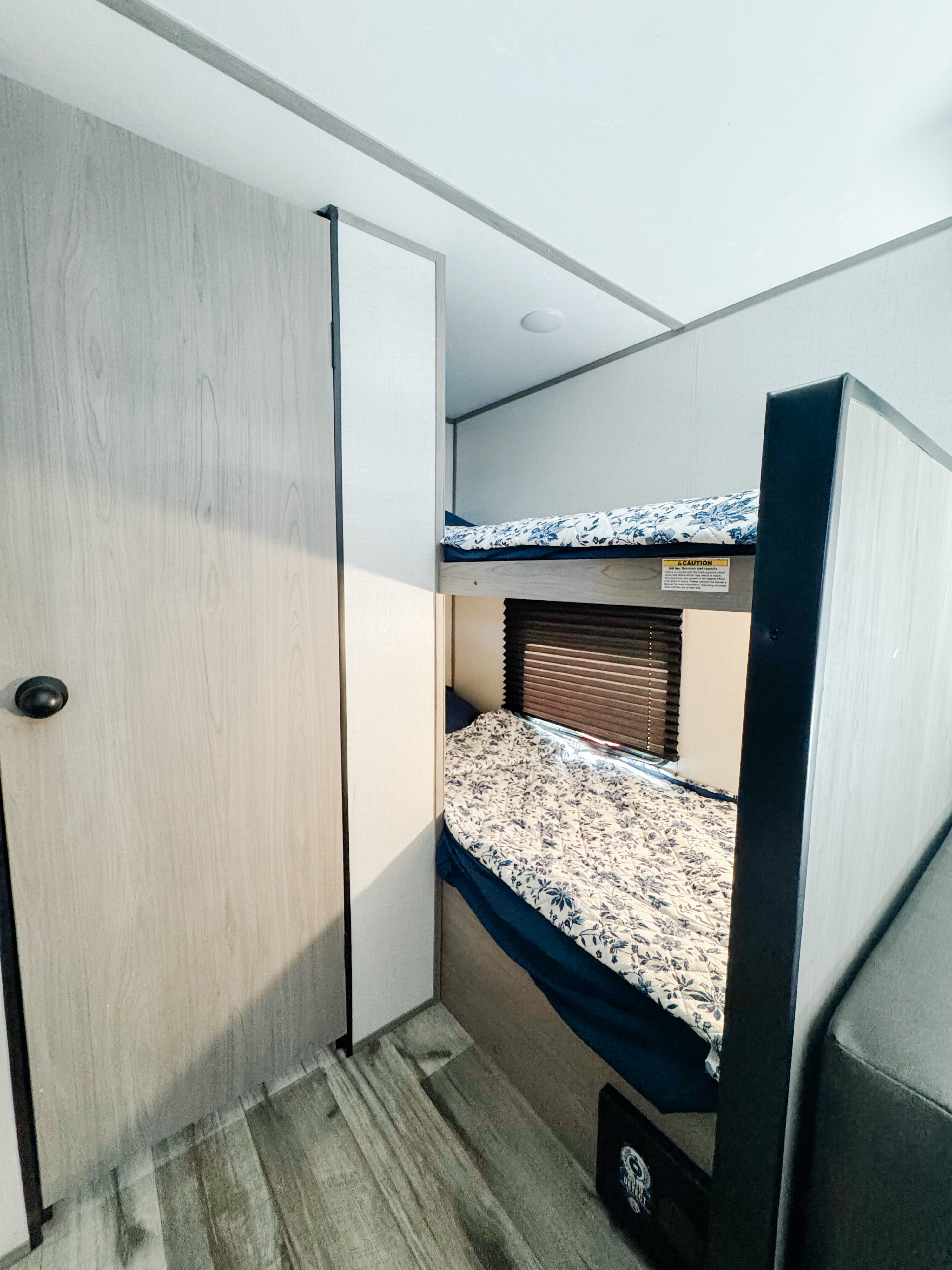 Cozy RV rental interior featuring two bunk beds with floral bedding, a wooden door, and a window with blinds.. Dutchmen Coleman Lantern LT 2023