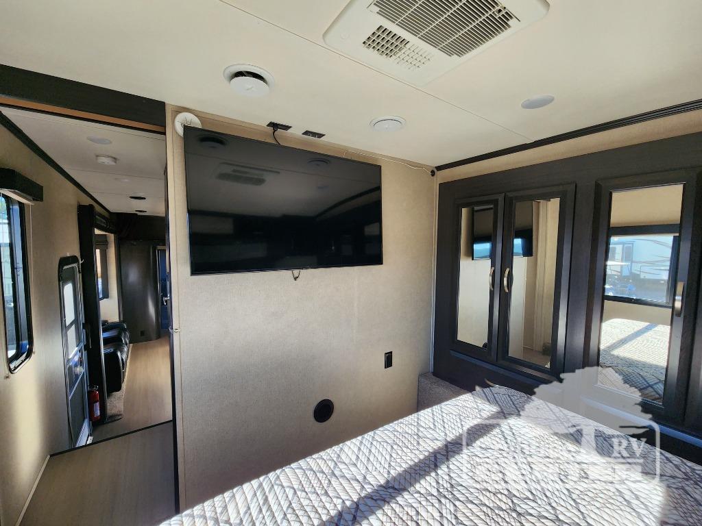 Modern RV rental interior: comfortable bedroom with large TV, AC, and a view of the spacious living area.. Keystone Voltage V3895 2017