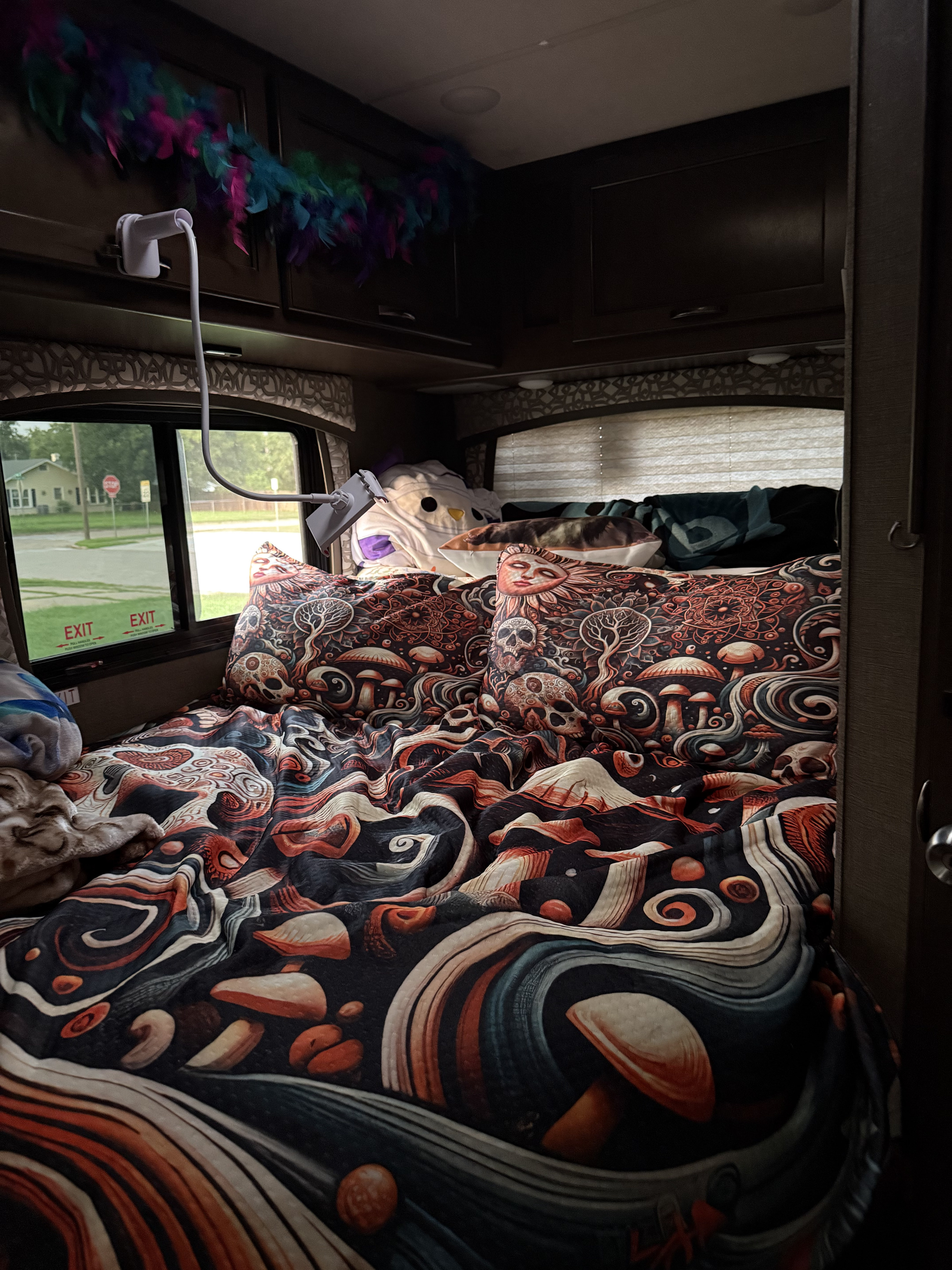 This inviting rv rental bed boasts unique, artistic bedding with mushrooms, skulls, and a sun face, flanked by a window view and vibrant decor.. Thor Chateau 2018
