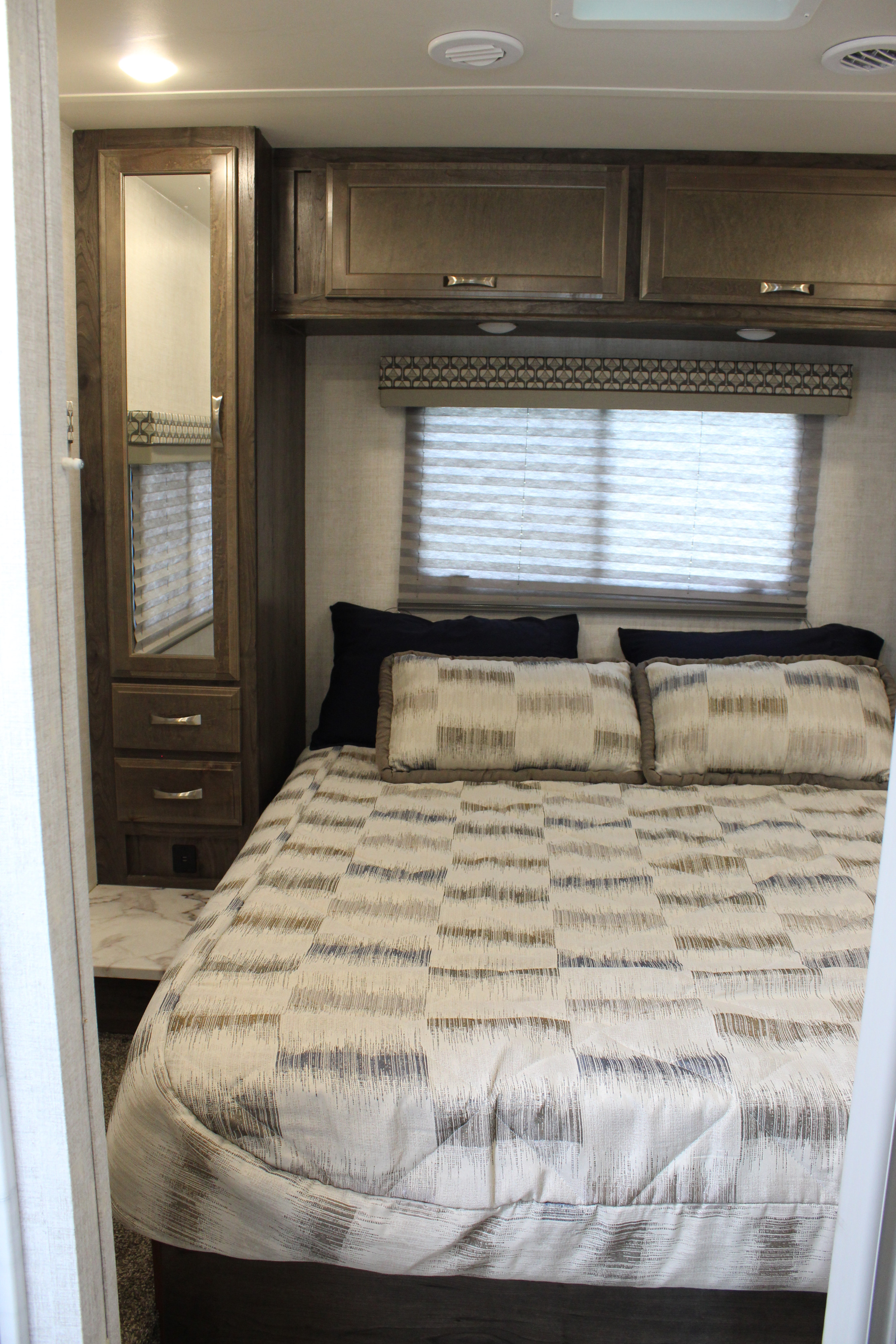 Comfortable RV rental bedroom featuring a patterned bed, mirrored cabinet, and compact overhead storage.. Gulf Stream Conquest 2021
