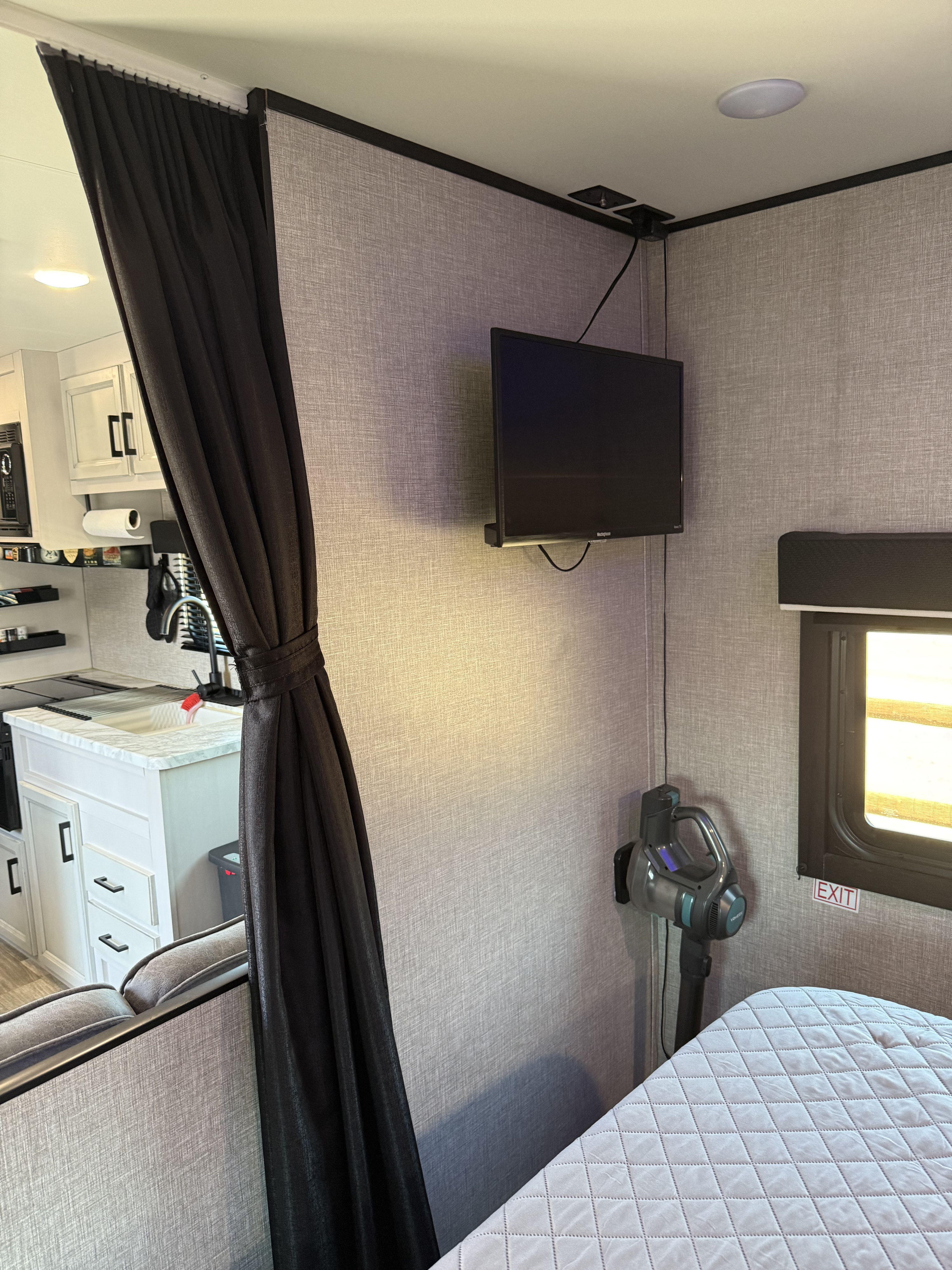 Cozy RV rental interior showing a compact kitchen, curtain partition, and wall-mounted TV/vacuum.. Jayco Jay Flight SLX 2022