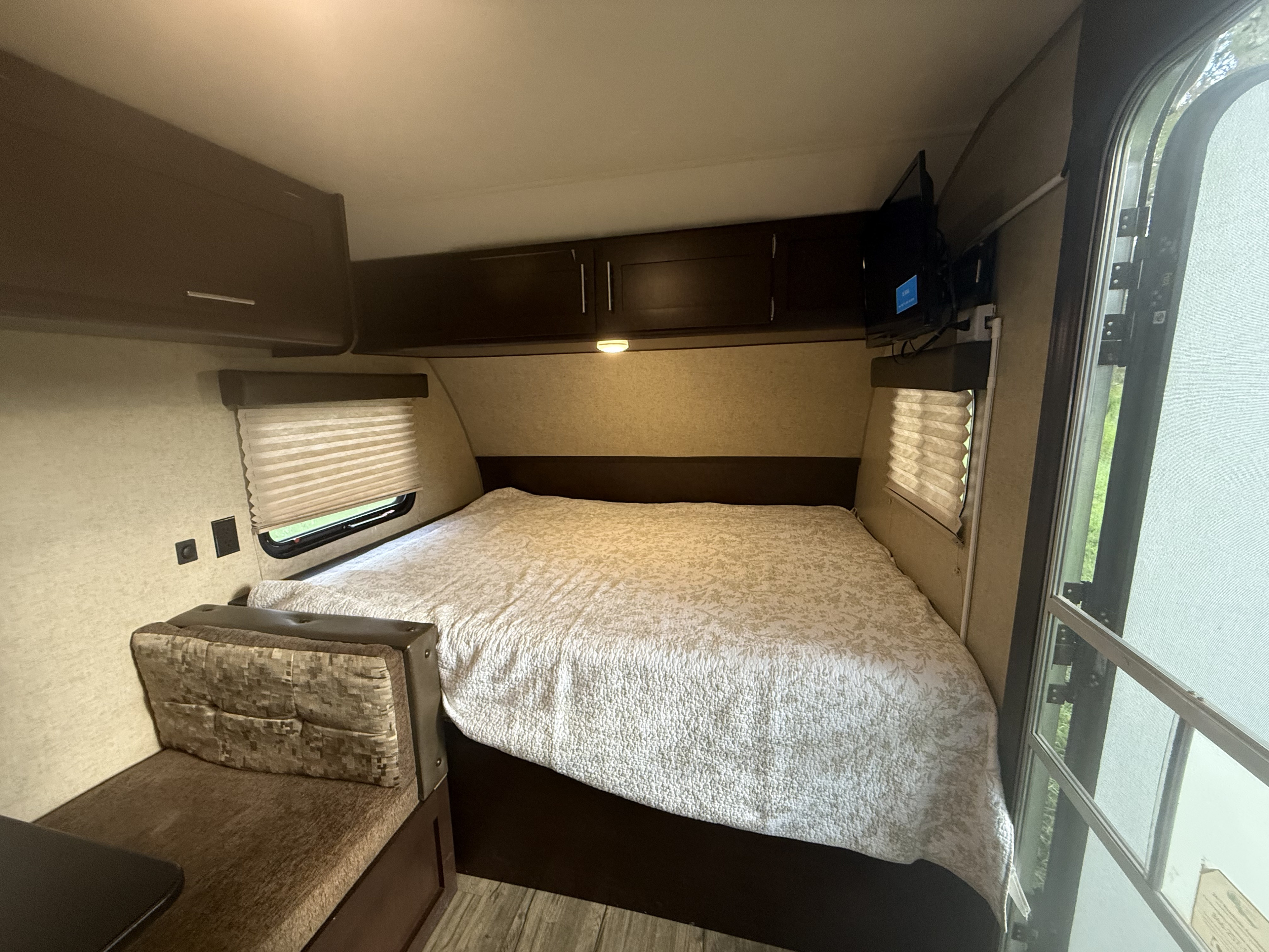 Cozy RV rental bedroom with a large bed, overhead cabinets, TV, and an open door for natural light.. Forest River Cherokee Wolf Pup Cascade 2017