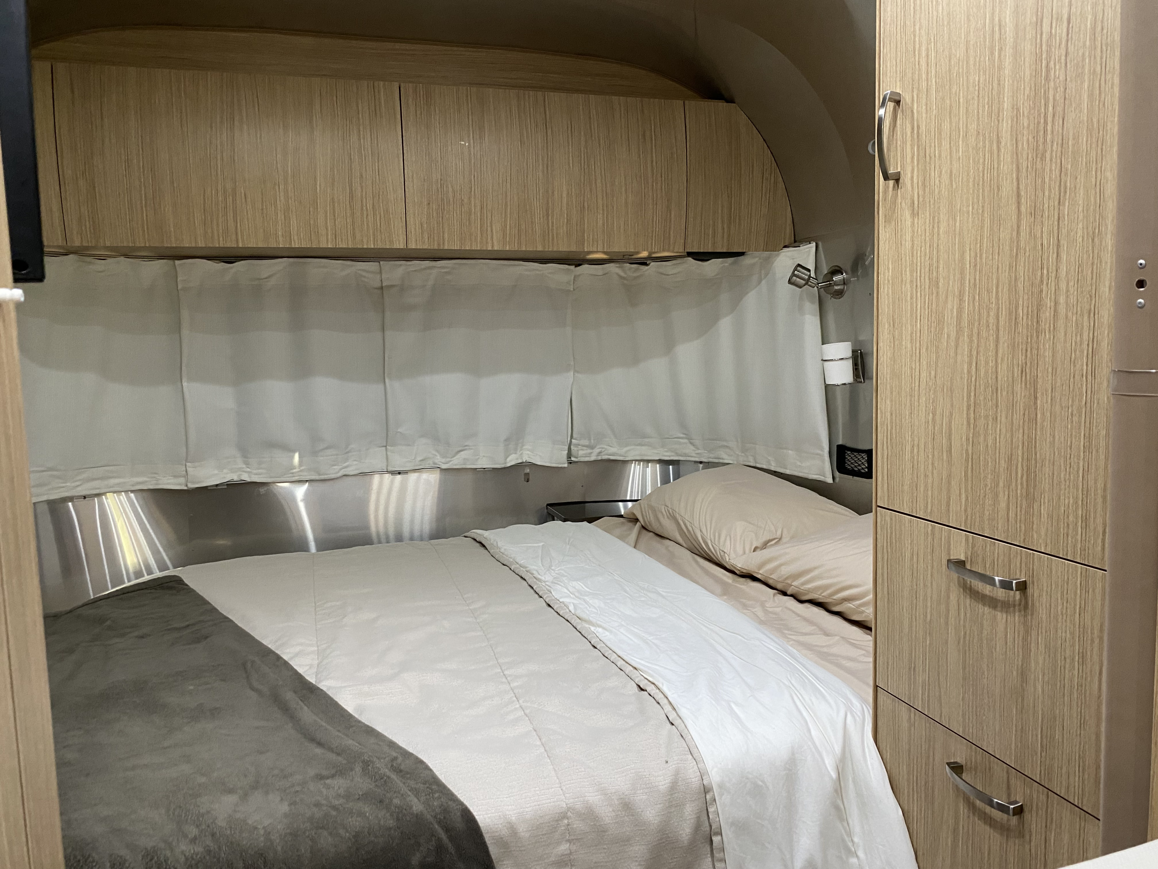 Experience comfort in this rv rental bedroom featuring light wood overhead cabinets, aluminum walls, and a neatly made bed.. Airstream Flying Cloud 2020