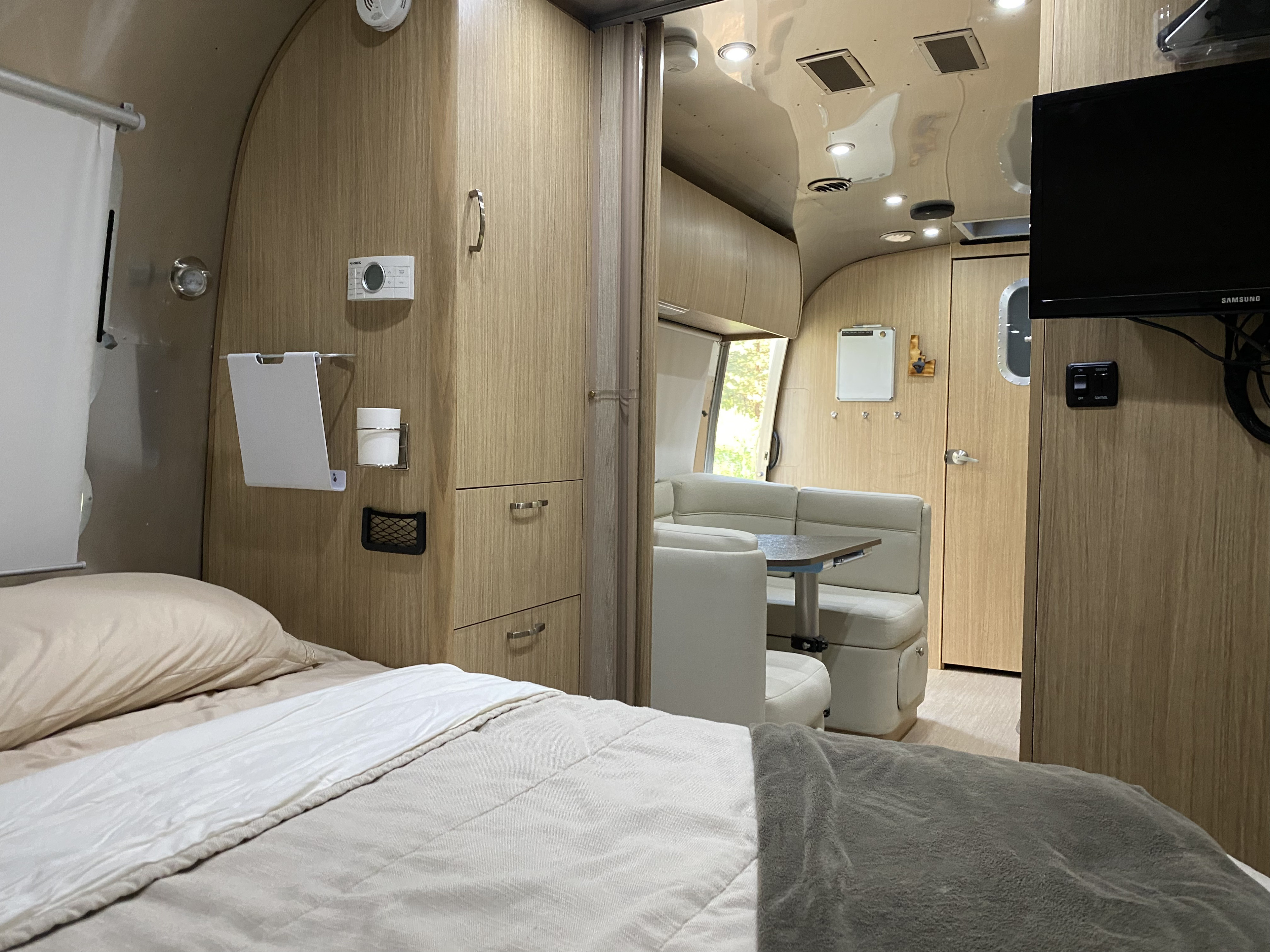 View from the bed inside a modern RV rental, featuring a dinette, wood cabinetry, and tech controls. Ideal for travel.. Airstream Flying Cloud 2020