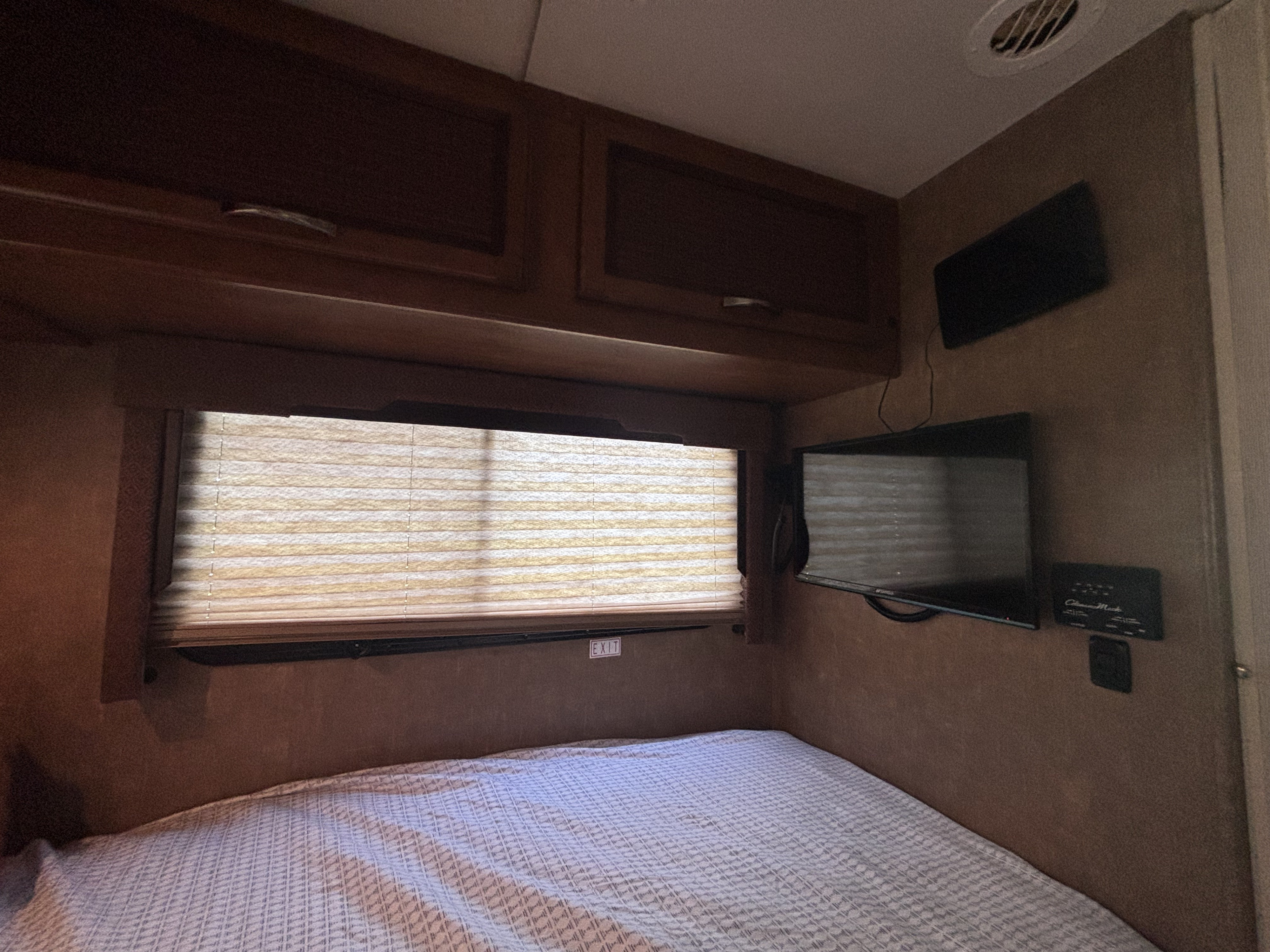 Cozy RV rental bedroom features a bed, window blinds, storage cabinets, and a wall-mounted TV.. Thor Axis 2015