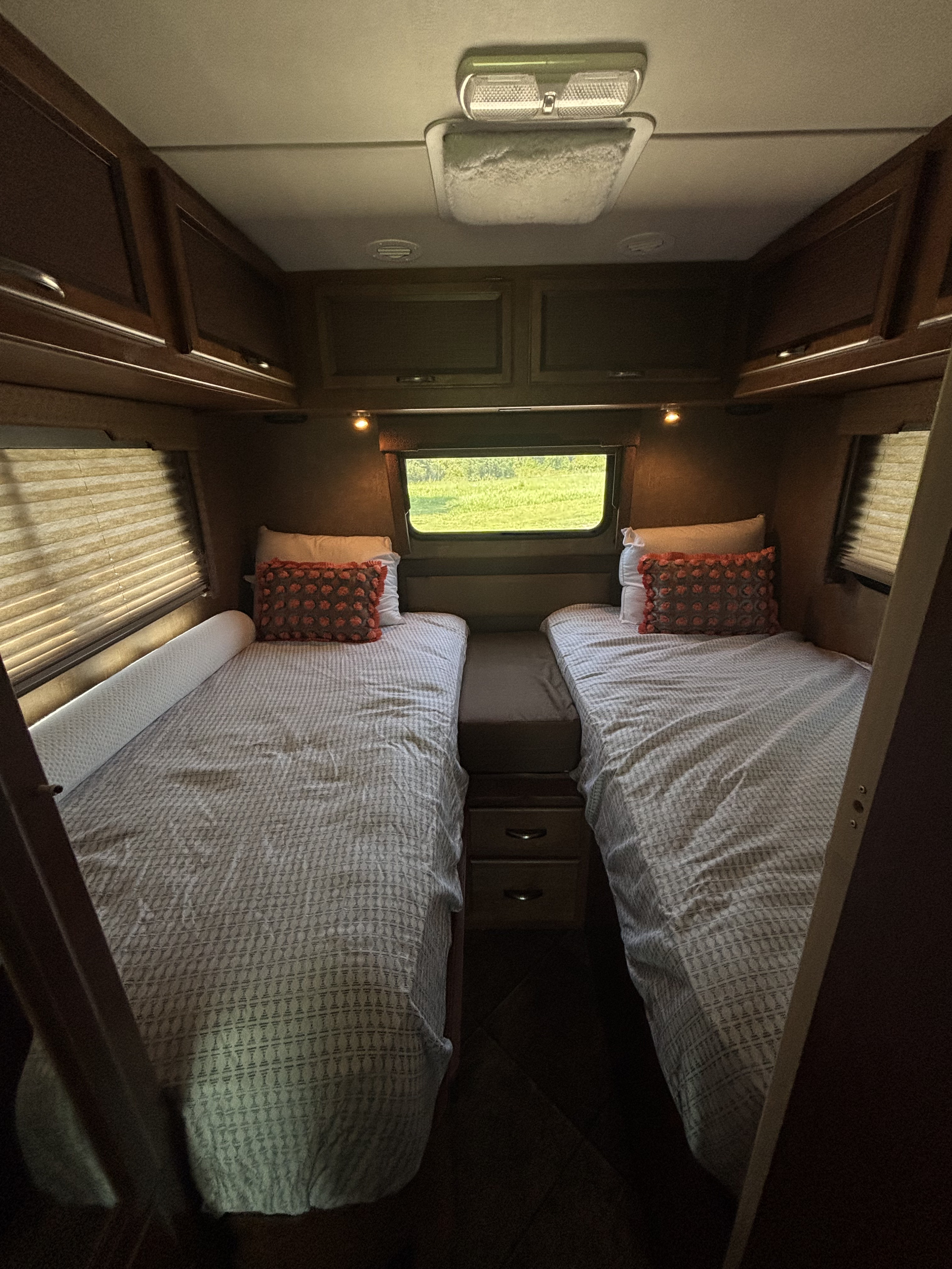 Inside an RV rental: two comfy twin beds with patterned sheets, overhead cabinets, and a scenic window view.. Thor Axis 2015