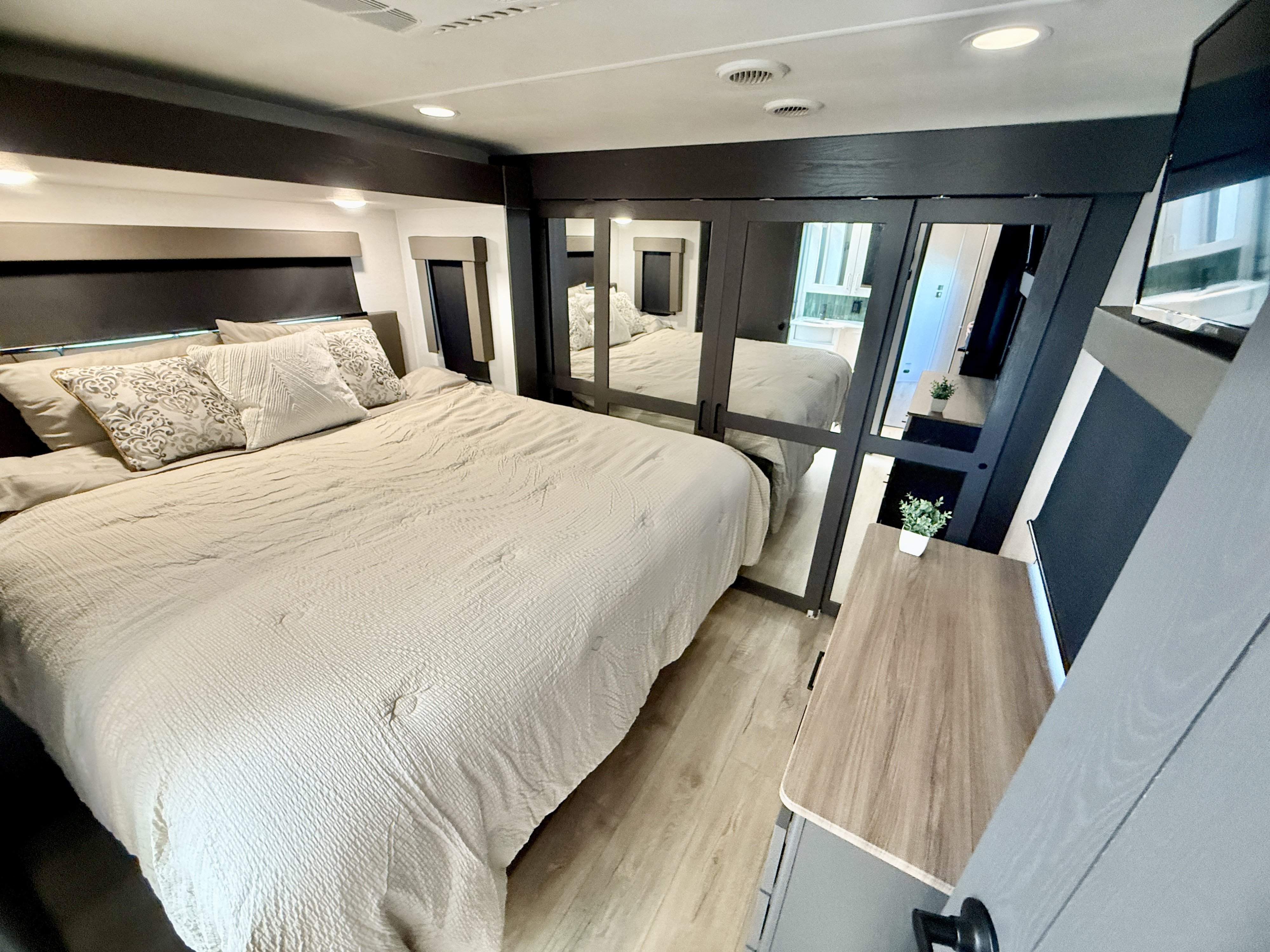 Modern RV rental bedroom features a large, comfy bed with light bedding, mirrored closet, and wall-mounted TV.. Aliance Valor 2024
