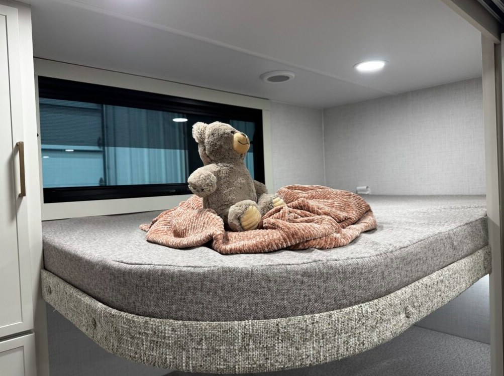 Cozy RV rental bunk with a teddy bear & pink blanket, ideal for family adventures. Bright, inviting interior.. Brinkley I294 2026