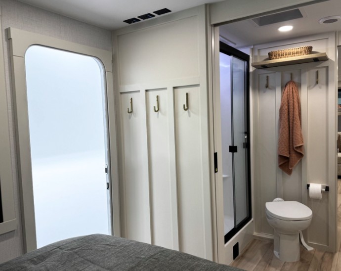 RV rental interior: bedroom view into a modern, compact bathroom with a shower, toilet, and handy wall hooks.. Brinkley I294 2026