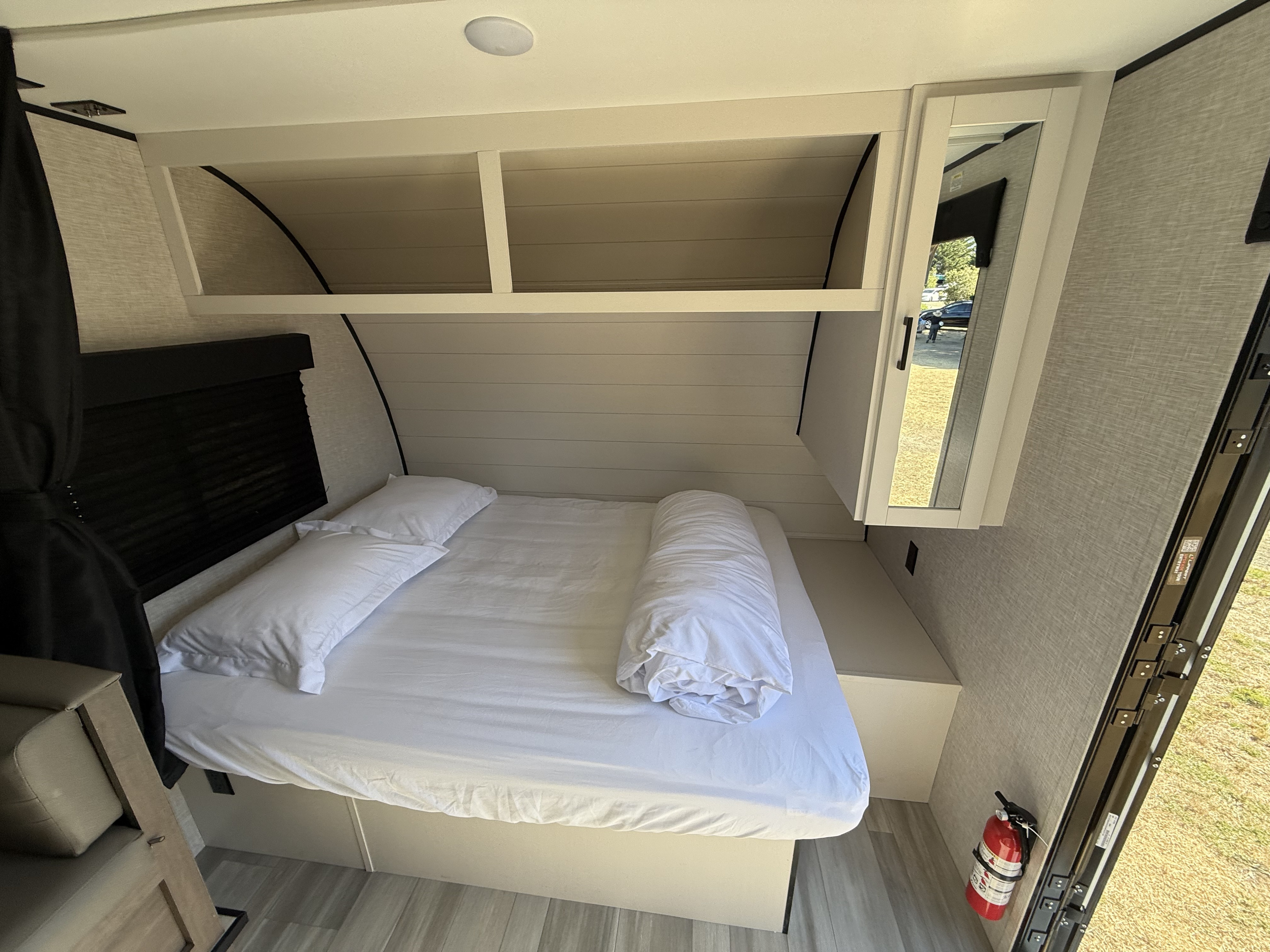 Interior of an RV rental bedroom showcasing a comfortable white bed, convenient overhead storage, and a mirrored cabinet.. Starcraft Autumn Ridge 2025