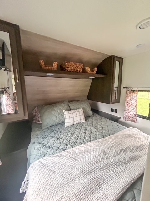 Relax in this cozy RV rental bedroom. Features a comfy bed with green quilted bedding, accent pillows, and overhead storage.. Jayco Jay Flight SLX 2021