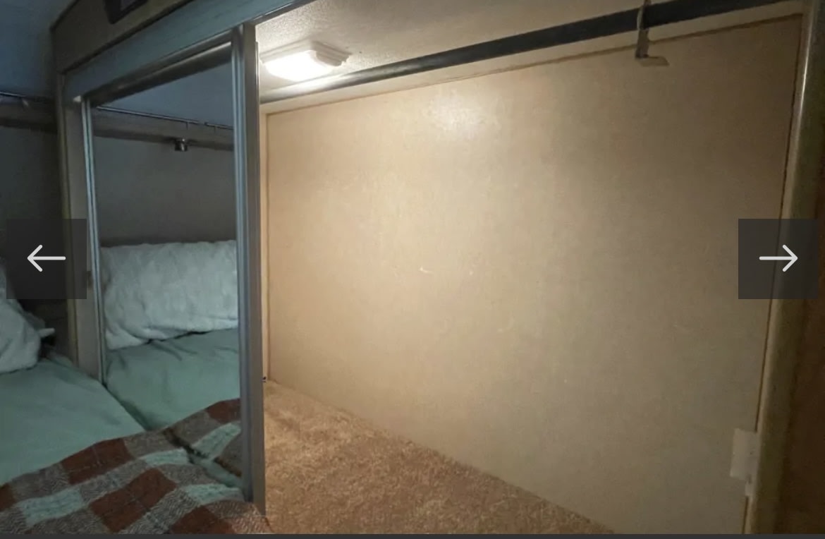 Cozy RV rental interior: bunk beds with light bedding and a plaid blanket behind a sliding door, next to a carpeted floor and ceiling light.. Lance 951 2007