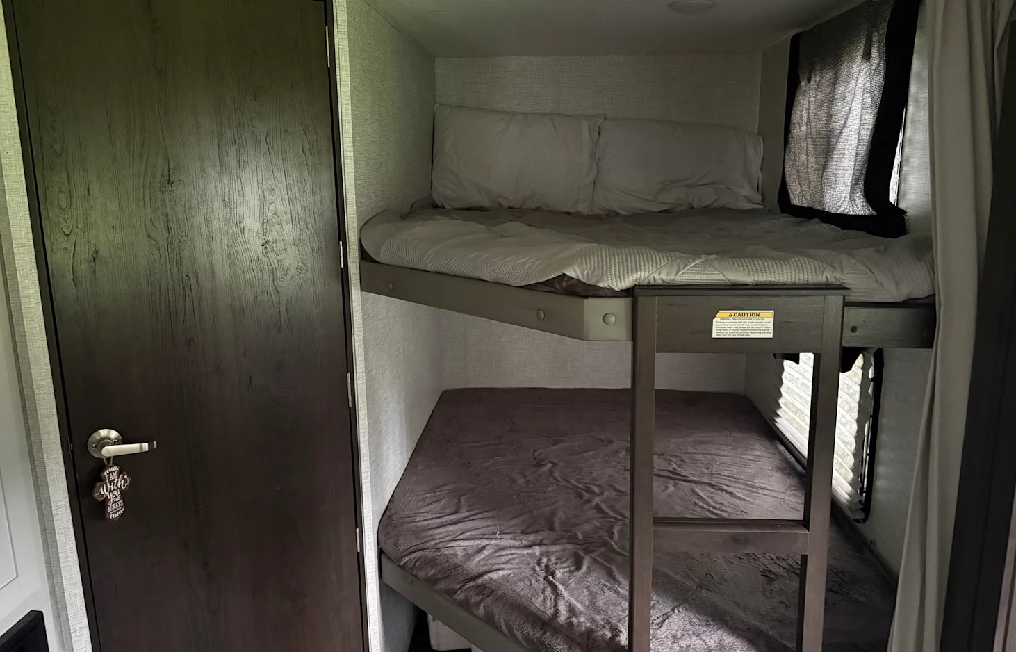 Inside an RV rental: two cozy bunk beds with light bedding, a dark door, and small windows, ready for a trip.. Keystone RV Bullet Crossfire 2021