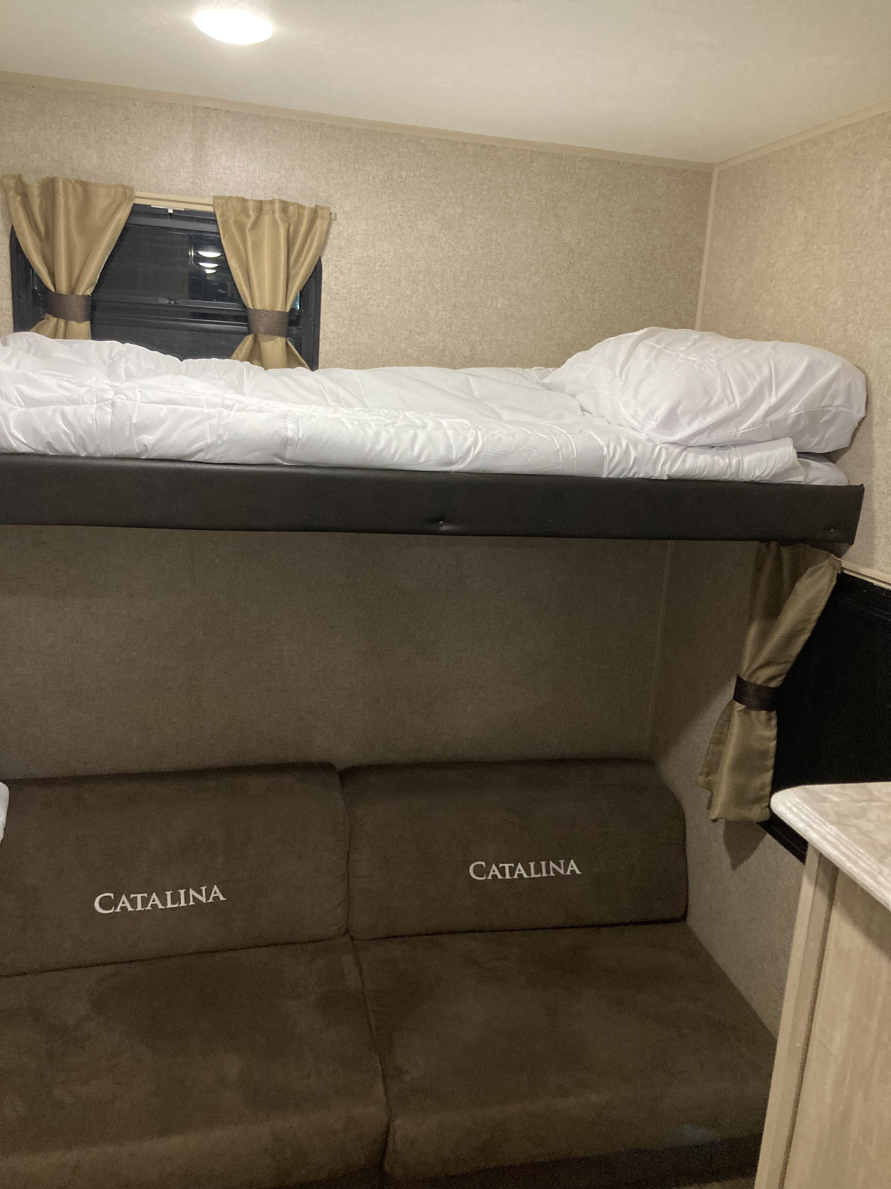 This RV rental offers cozy bunk beds with white bedding above a "CATALINA" sofa, a great space for rest and relaxation.. Coachmen Catalina Legacy 2019