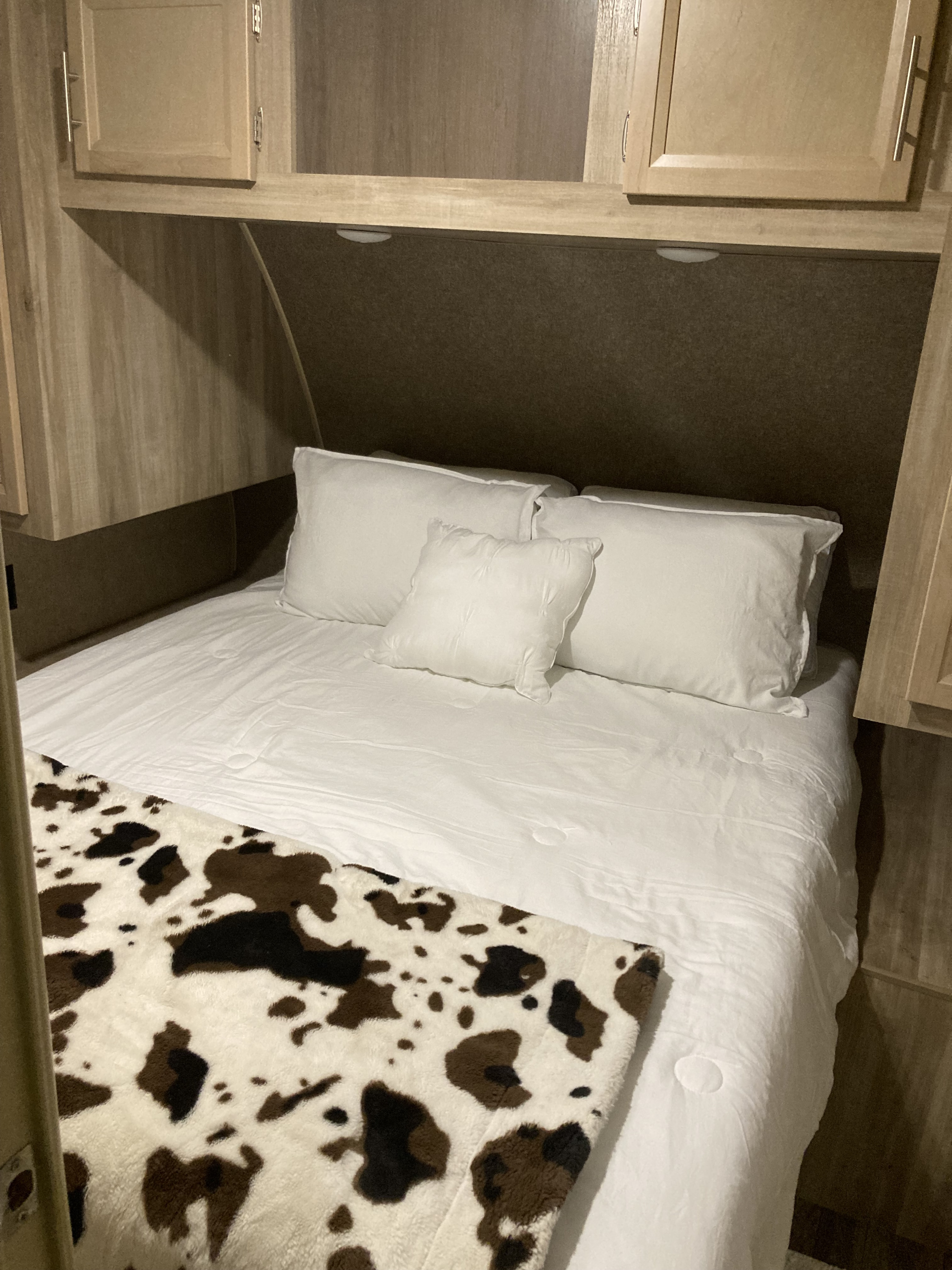 Cozy RV rental bedroom featuring a comfy bed with white linens, multiple pillows, and a fun cow print throw.. Coachmen Catalina Legacy 2019
