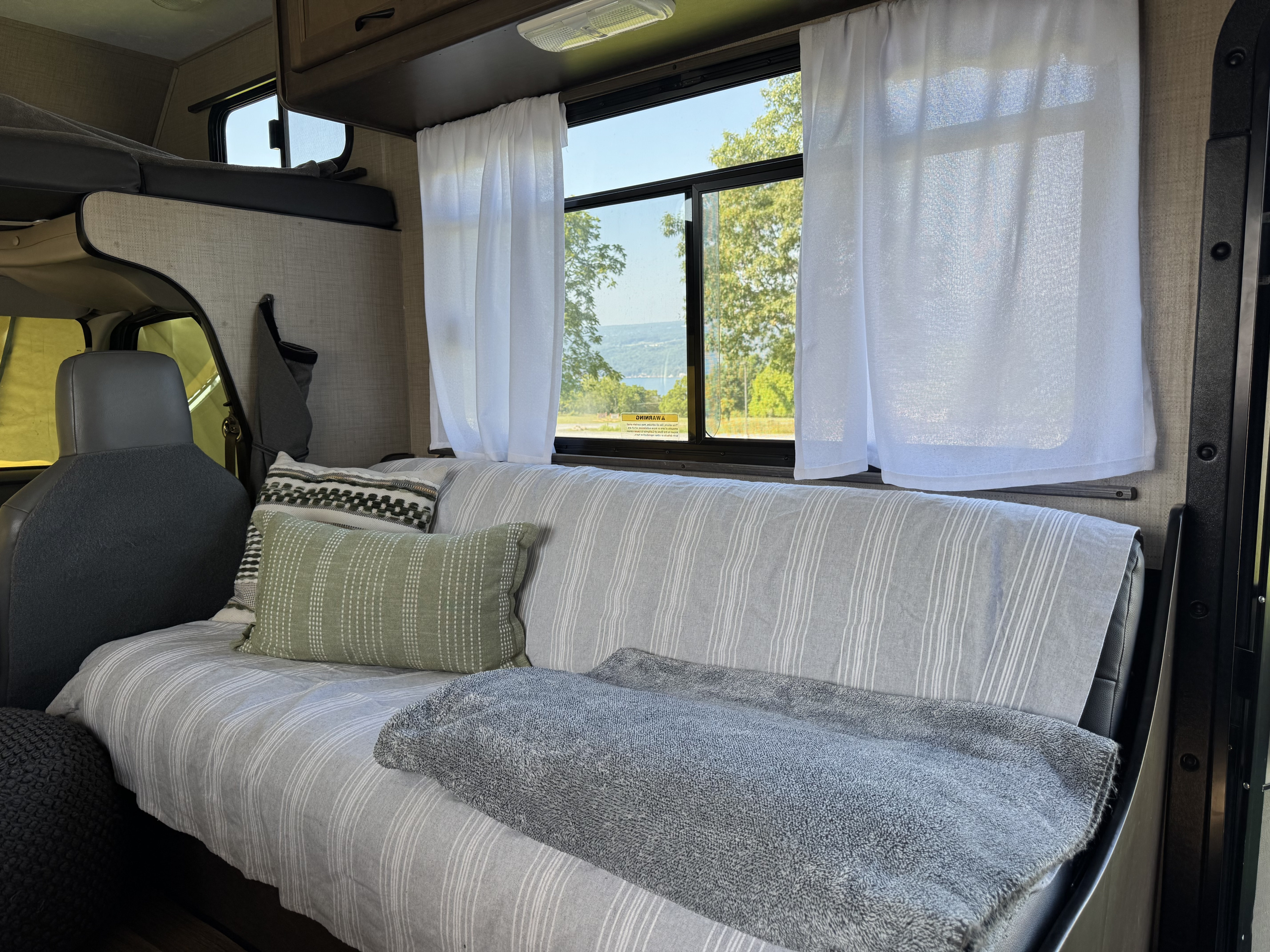 Cozy RV rental interior with striped seating/bed, pillows, and a scenic window view of nature.. Thor Majestic 2019
