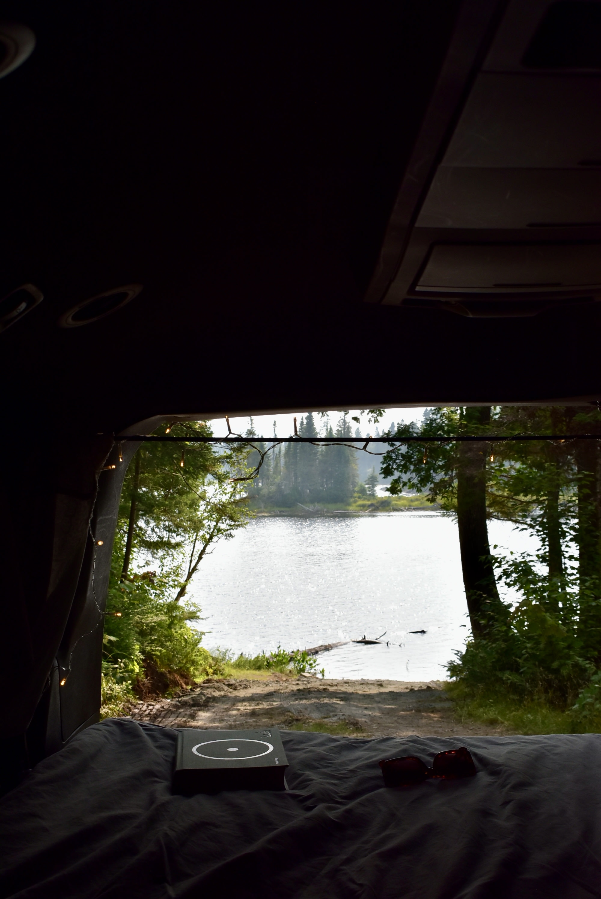 RV rental: Peaceful lakeside view from inside, showing a cozy bed with a book, sunglasses, and lush nature outside.. Dodge Dodge Grand Caravan GT 2017 2017
