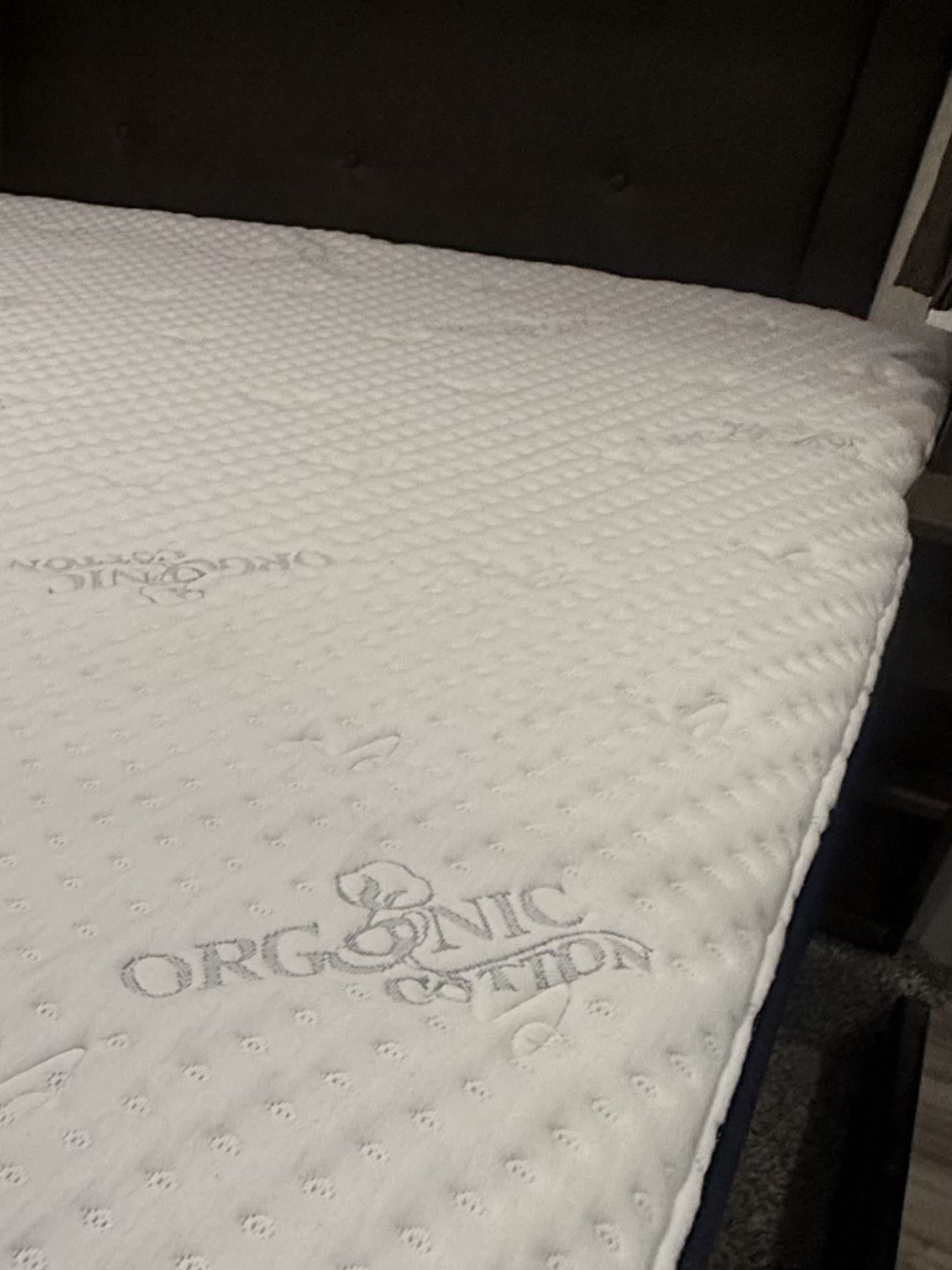 Comfortable, white quilted mattress with "ORGANIC COTTON" text in an RV rental. Features a dark headboard for a cozy sleep setup.. Keystone RV Cougar 2019