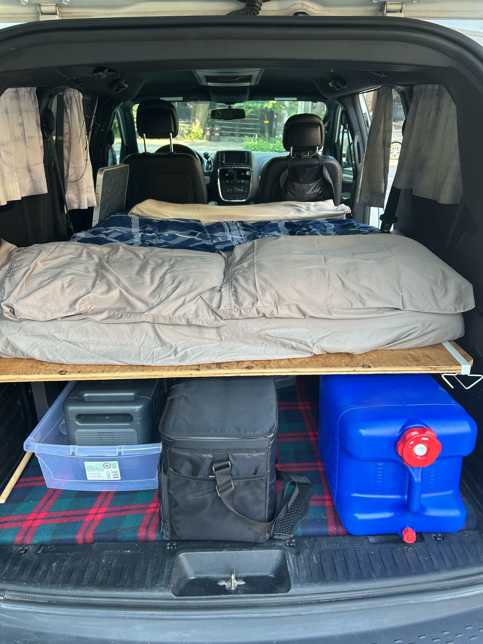Inside an RV rental: a cozy van camping setup with a portable bed platform, storage bin, cooler, and water jug. Ready for adventure!. Dodge Dodge Grand Caravan GT 2017 2017