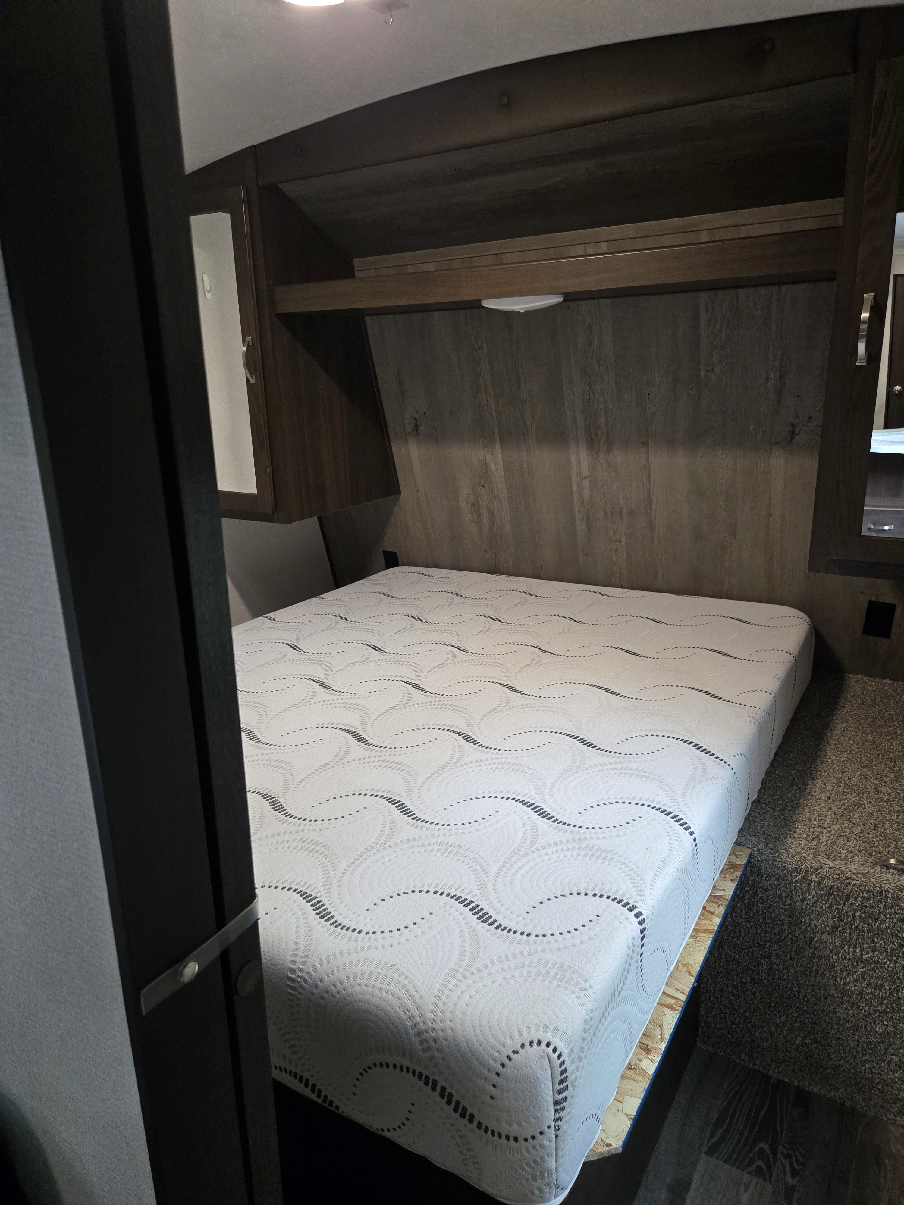 Your next RV rental offers a comfy bedroom with a patterned mattress, wood accents, and convenient overhead storage.. Keystone RV Springdale 2020